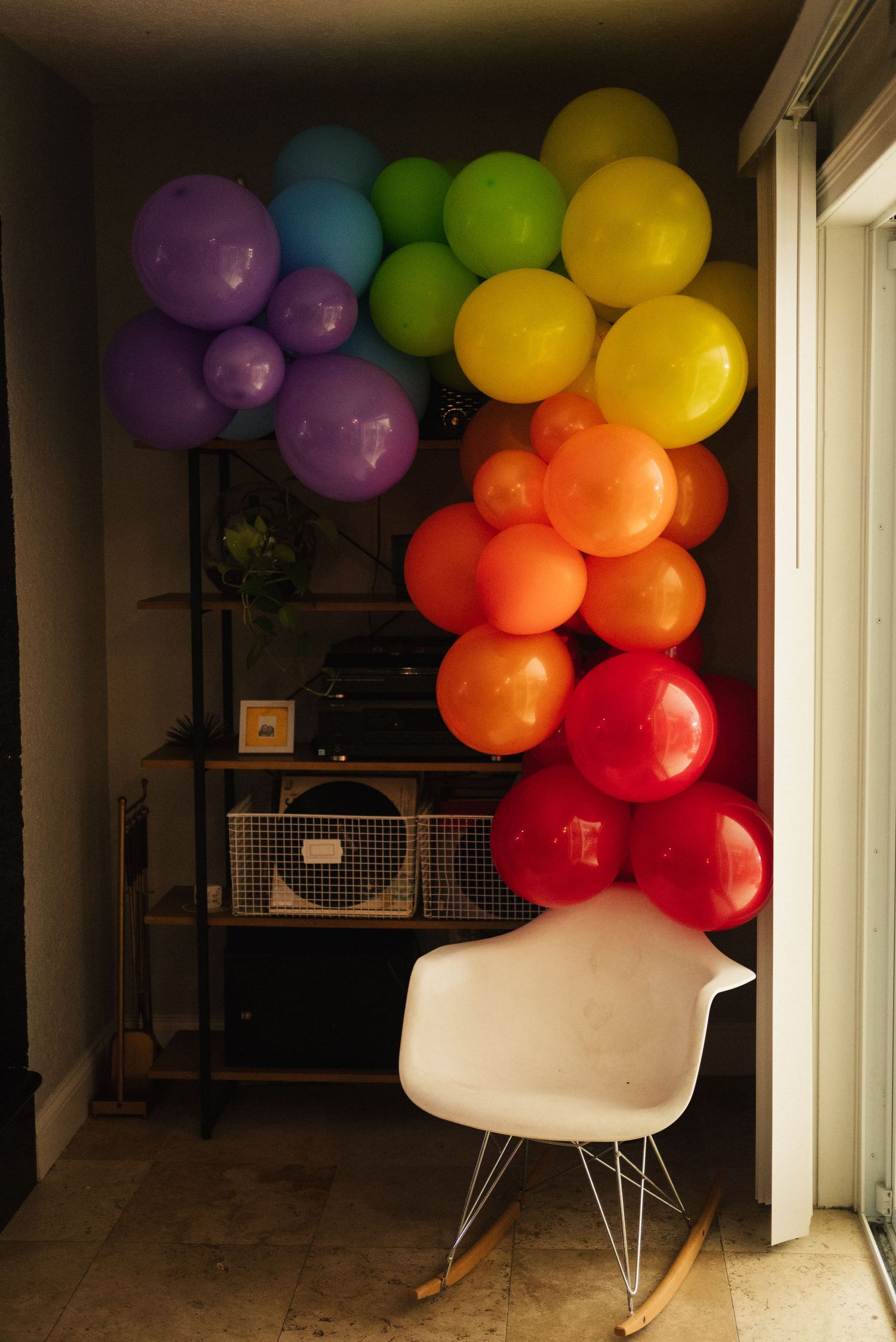 Rainbow balloon arch display next to white modern chair in room corner.