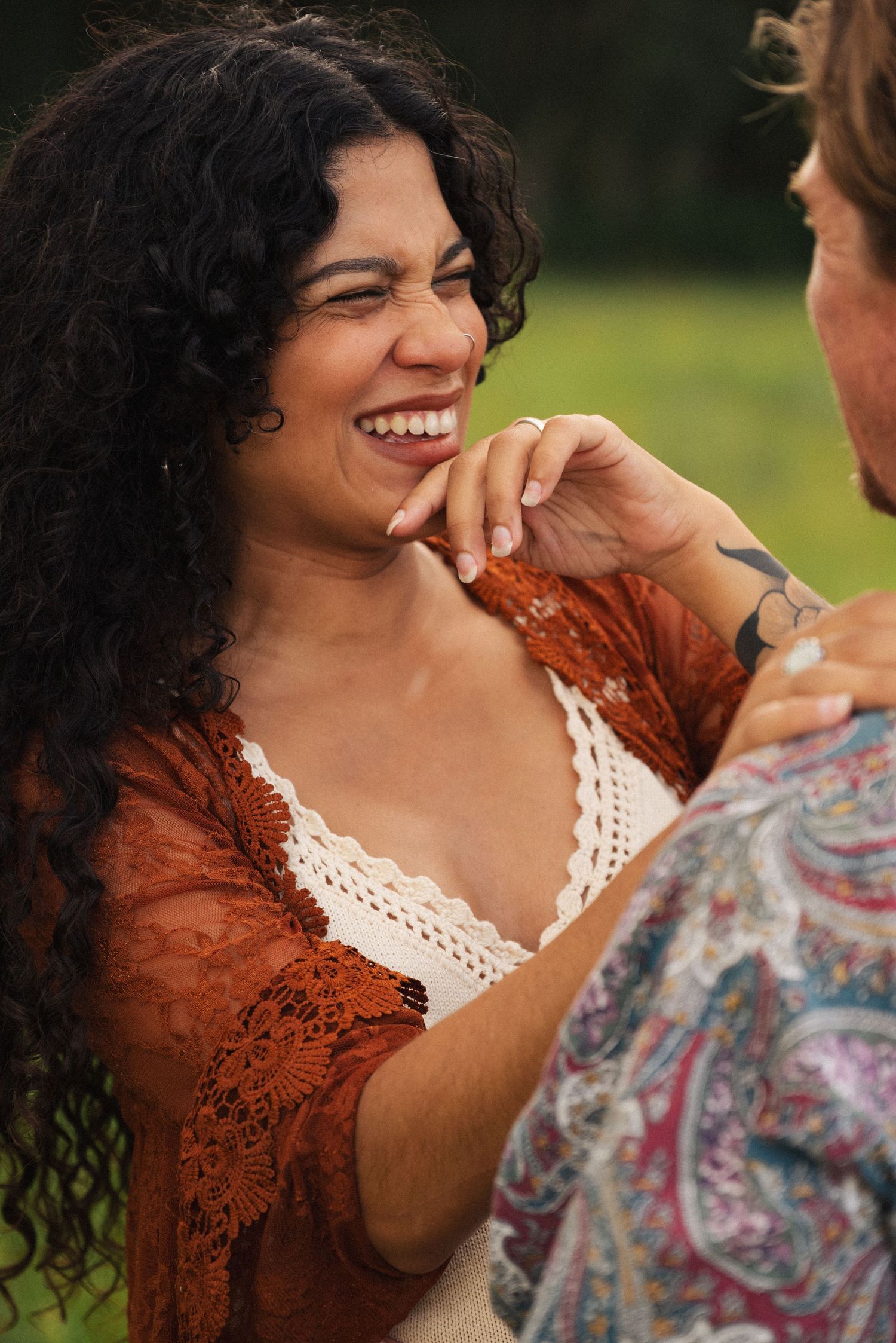 A couple shares a joyful moment in a field wearing rustic attire.