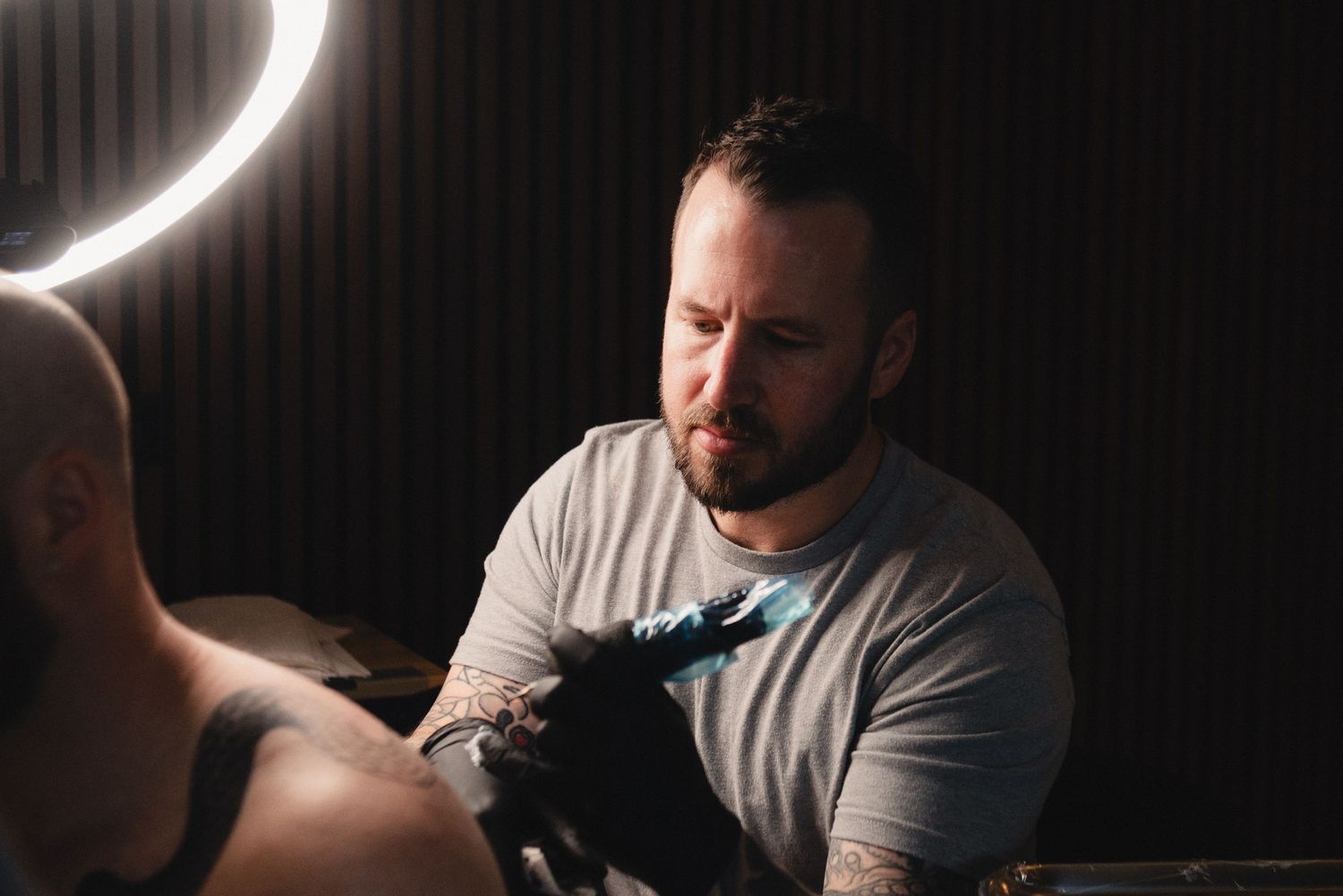 Professional tattoo artist concentrates while working in a dimly lit studio setting.
