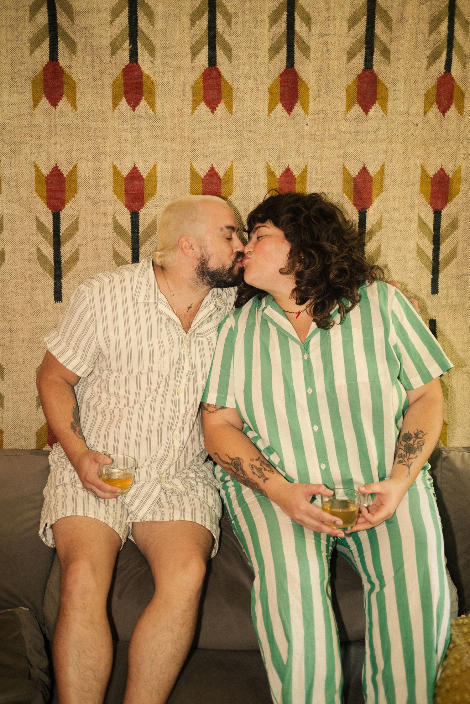 Two people in coordinating striped and white outfits sitting close together on couch.