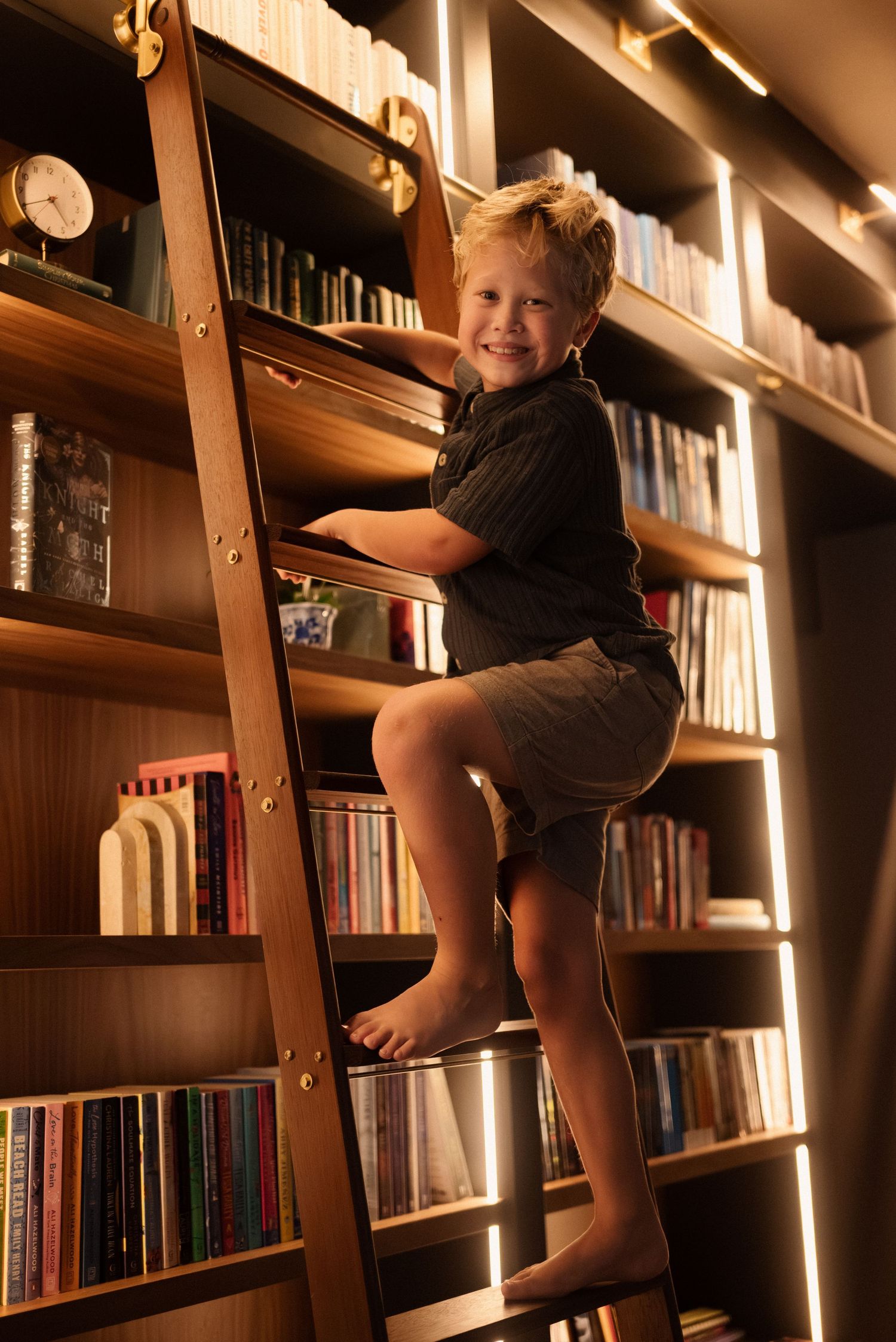Photos of someone climbing and sitting on wooden bookshelves filled with books and illuminated by warm lighting.