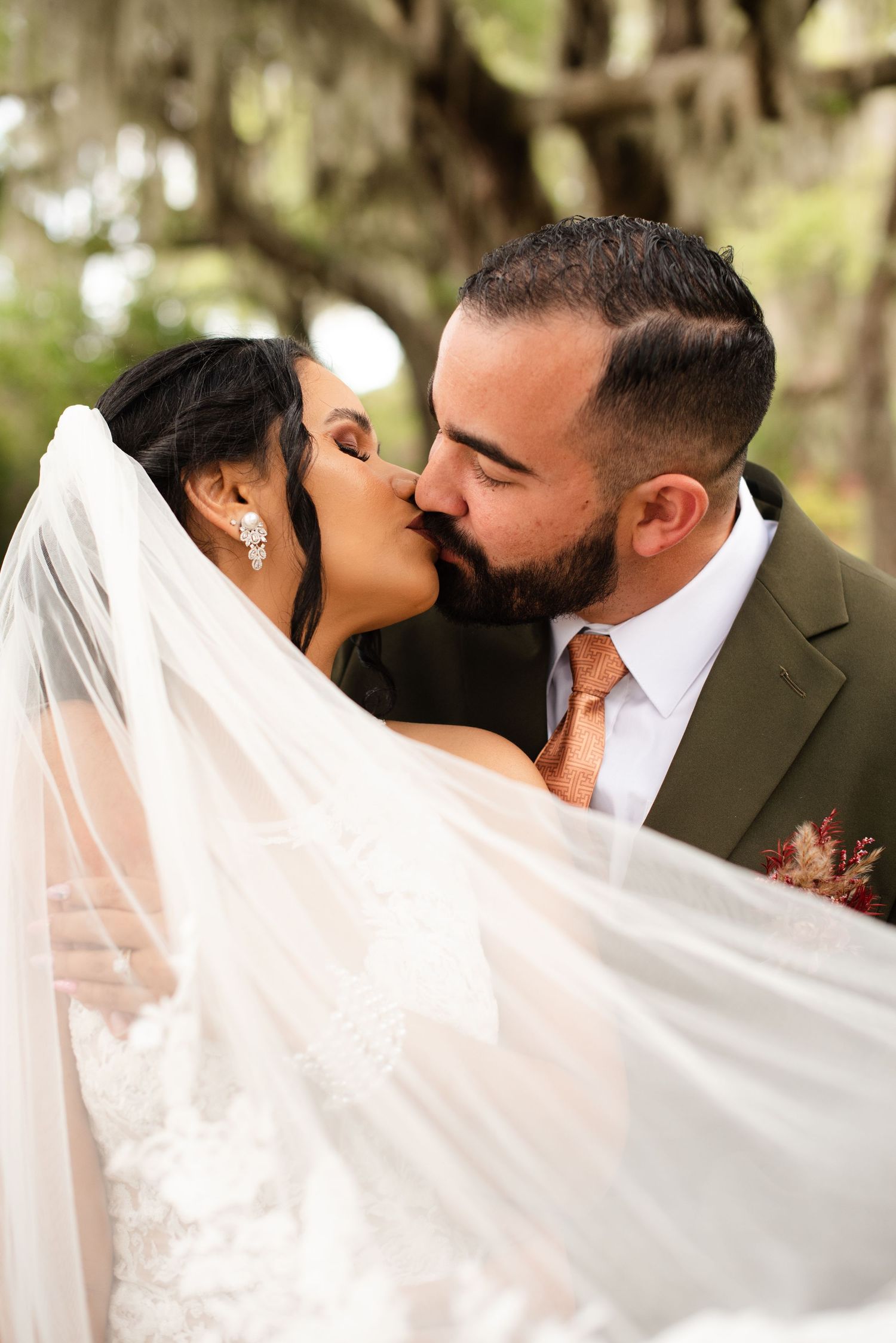Romantic wedding portrait under Spanish moss with flowing veil in natural light.