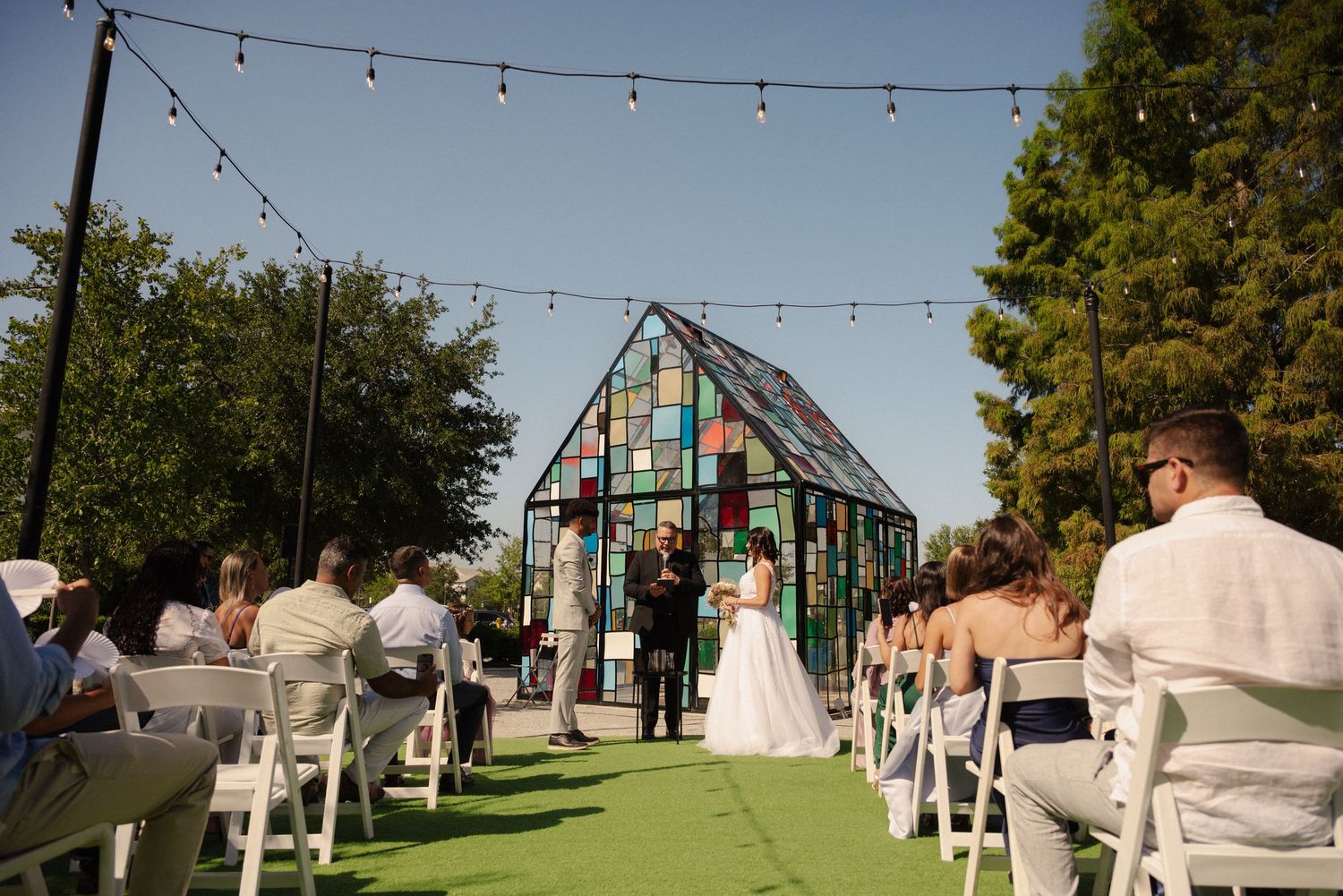 An outdoor wedding venue with string lights and decorative elements under blue sky.
