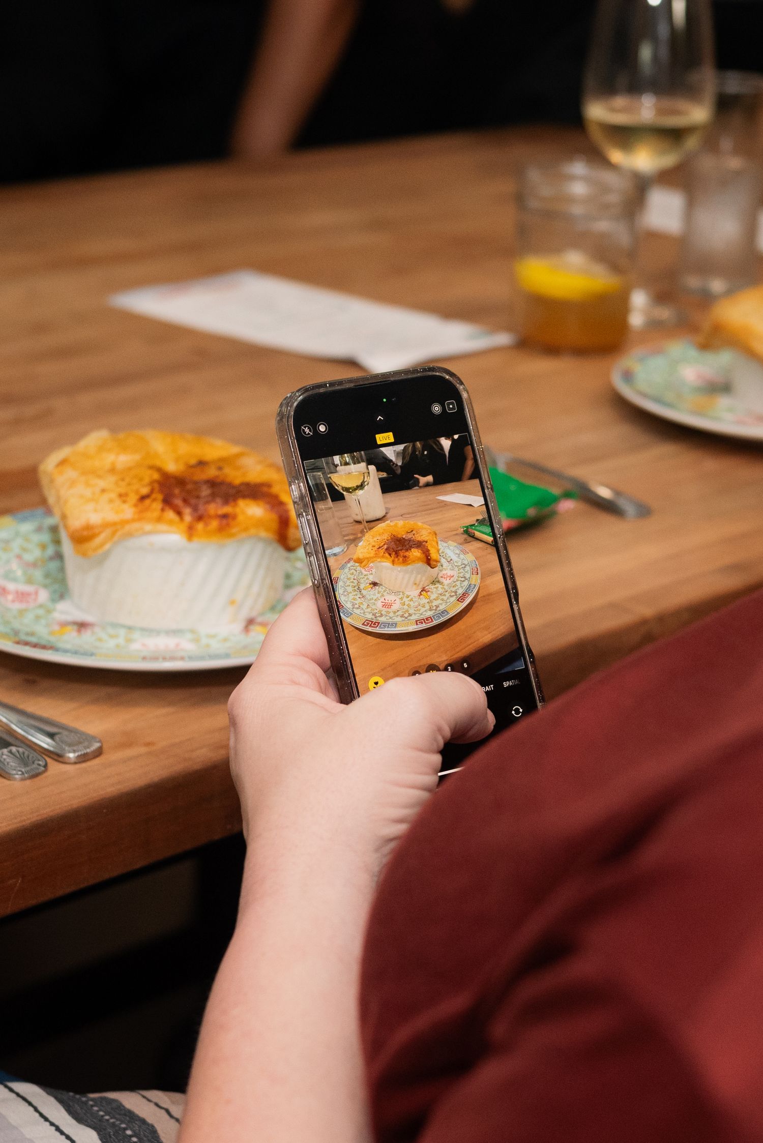 Someone taking food photos with a smartphone at a restaurant table.