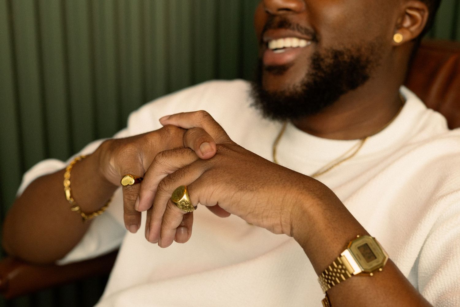 Individual wearing white t-shirt and gold accessories relaxing in brown leather chair.