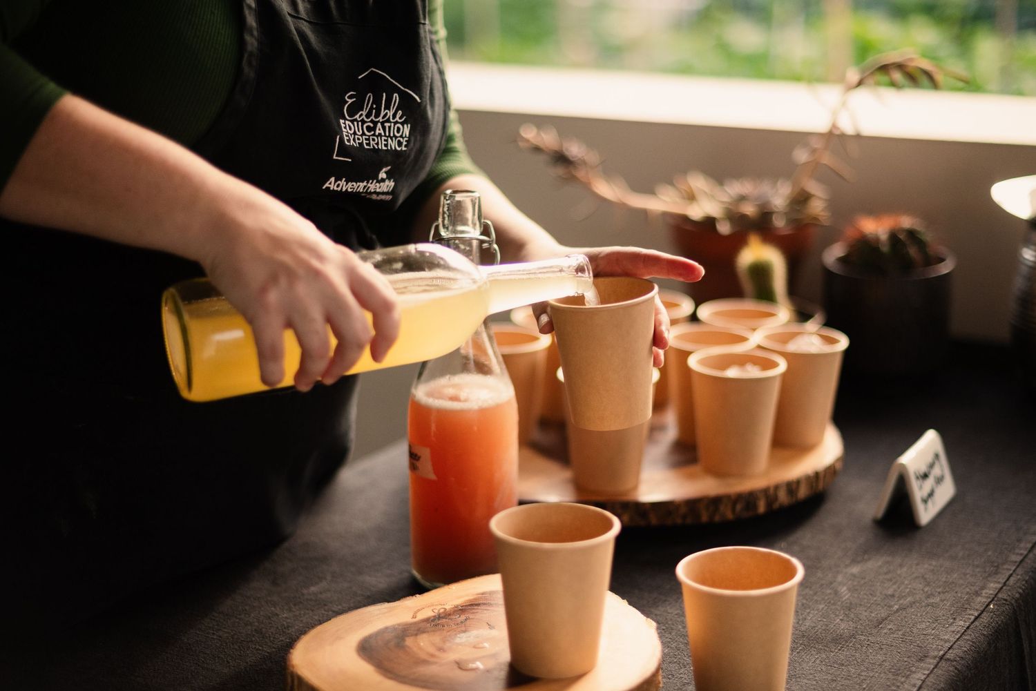 Drinks being poured into clay cups on a wooden serving board at an outdoor event.