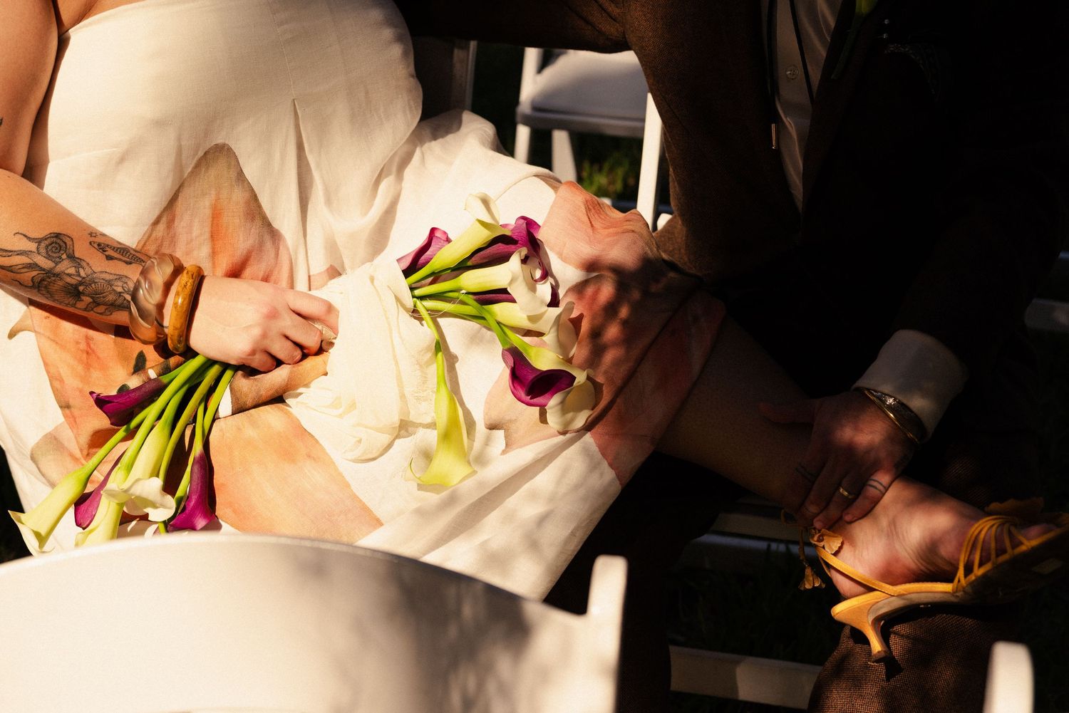 Hands holding and arranging colorful calla lily flowers against a white dress.