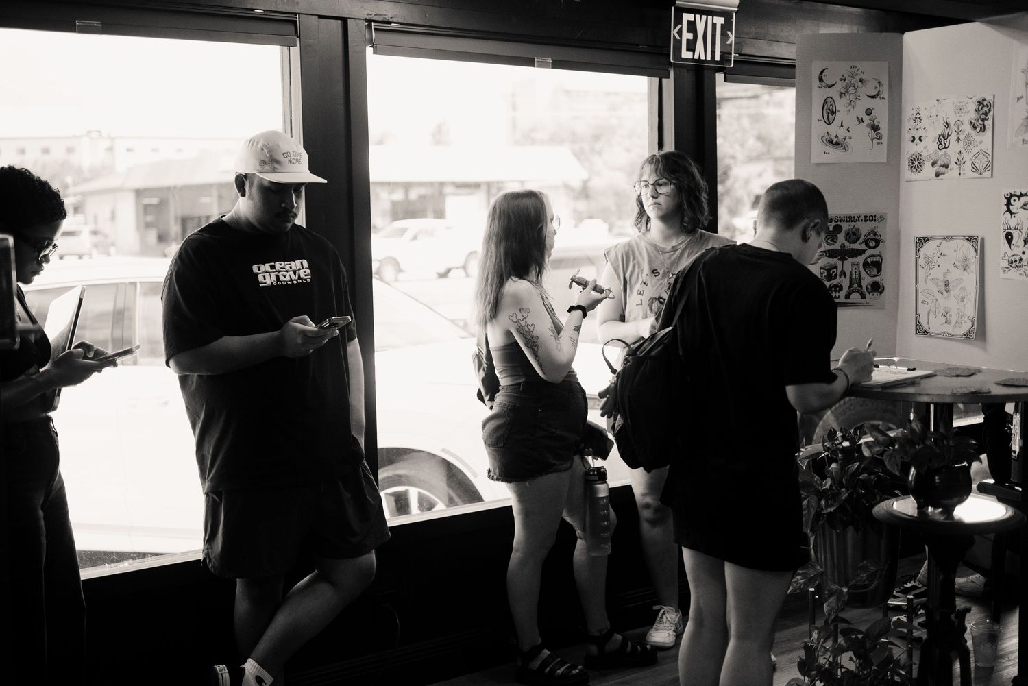Customers and staff interact inside a dimly lit tattoo shop with artwork displayed on the walls.