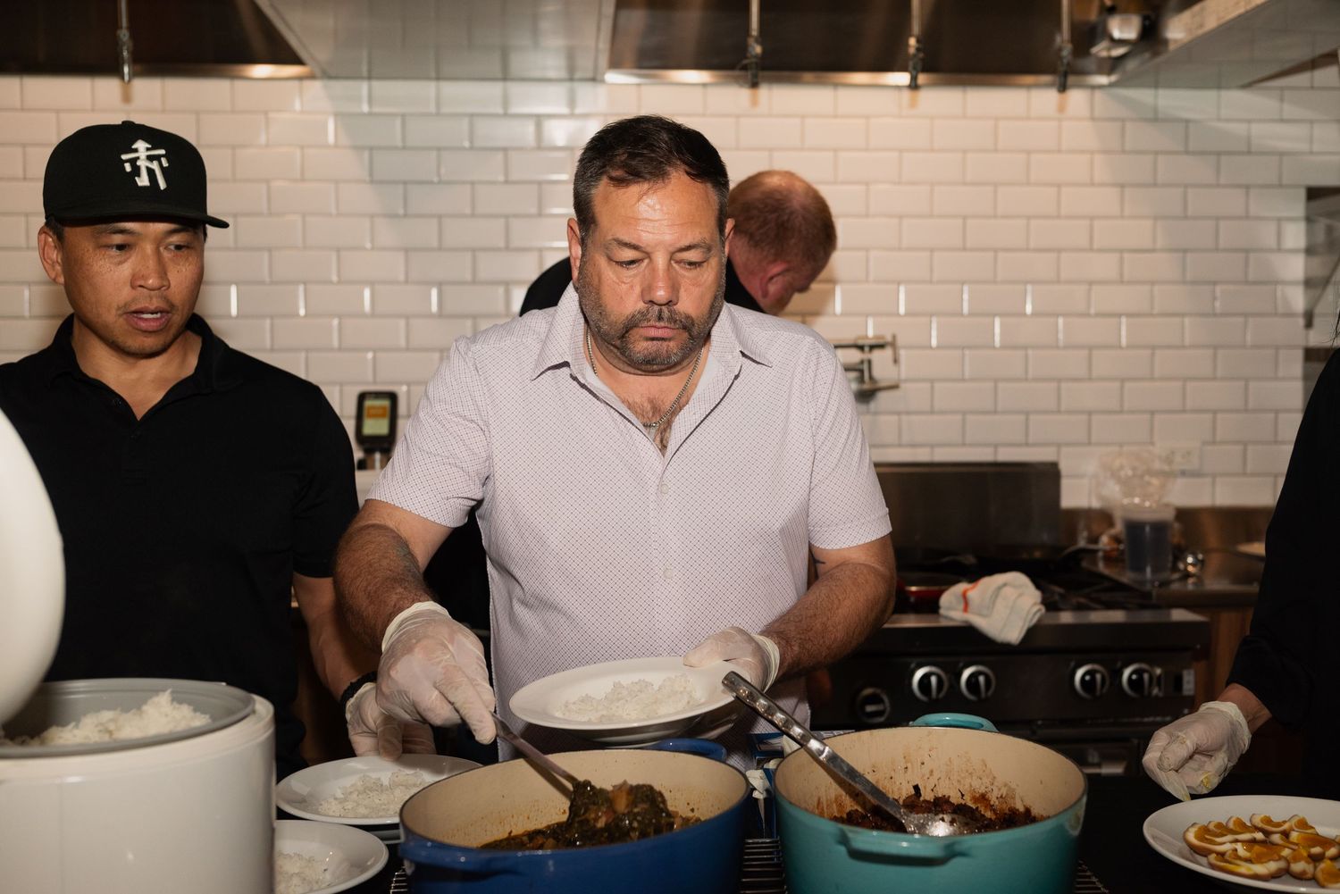 Kitchen staff plating dishes in a restaurant with white subway tile walls.
