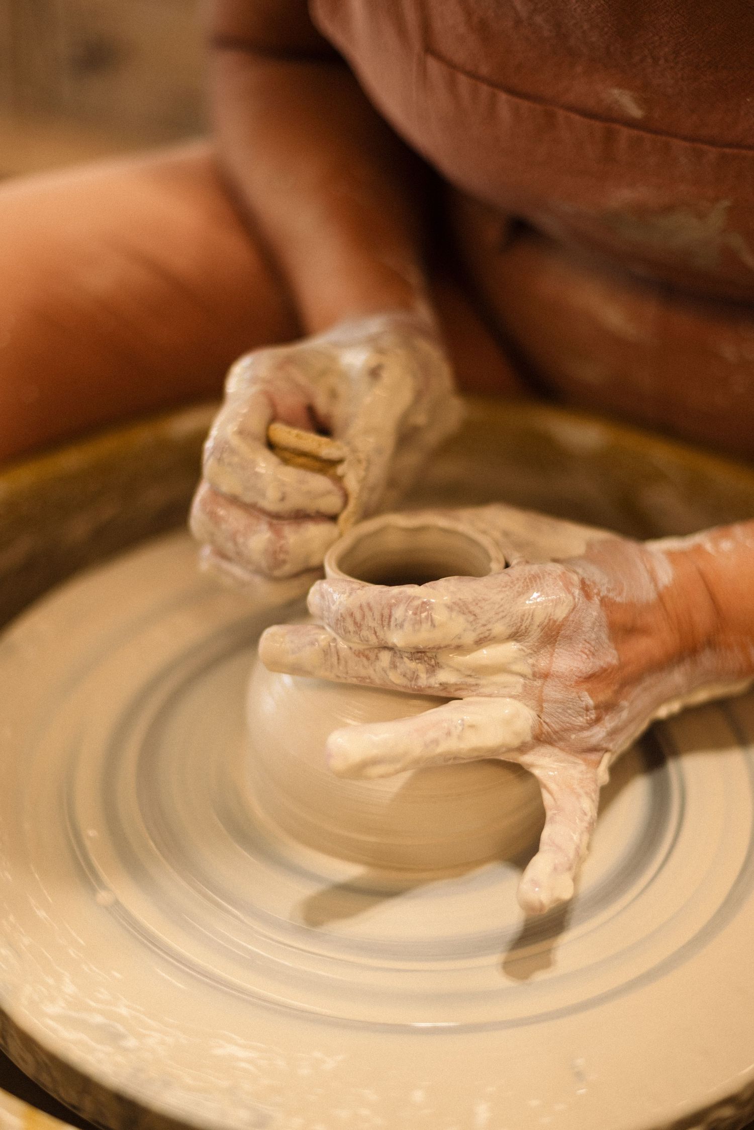 Clay-covered hands shaping a vessel on a pottery wheel.