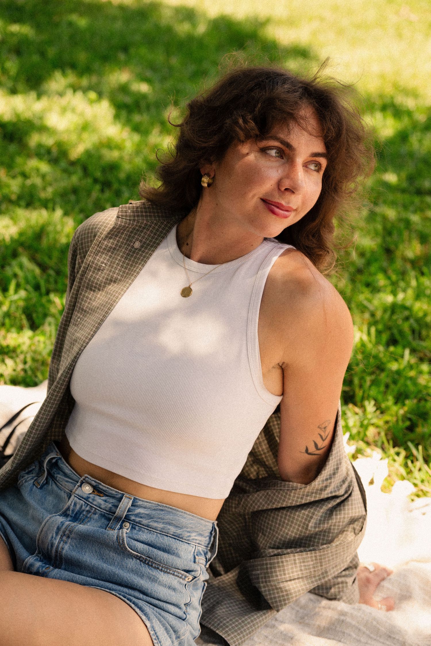 Summer fashion outfit with white crop top, denim shorts and plaid shirt in outdoor setting.