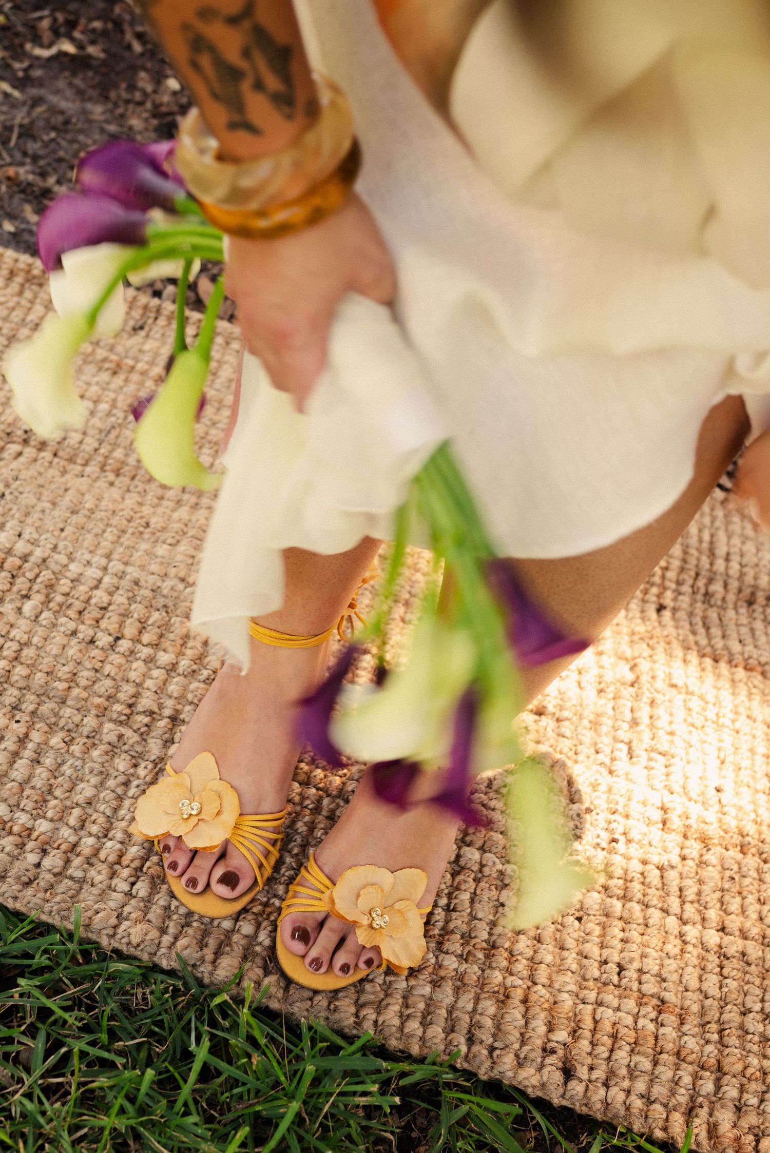 Close-up of bare feet on a woven mat with purple calla lilies in the foreground.