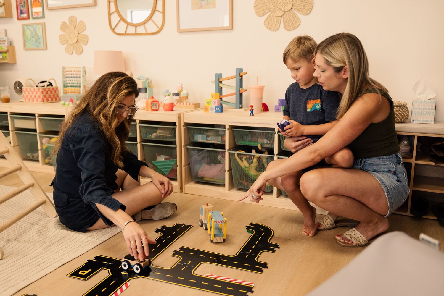 Children playing with toys on a wooden floor in a playroom with storage cubbies.