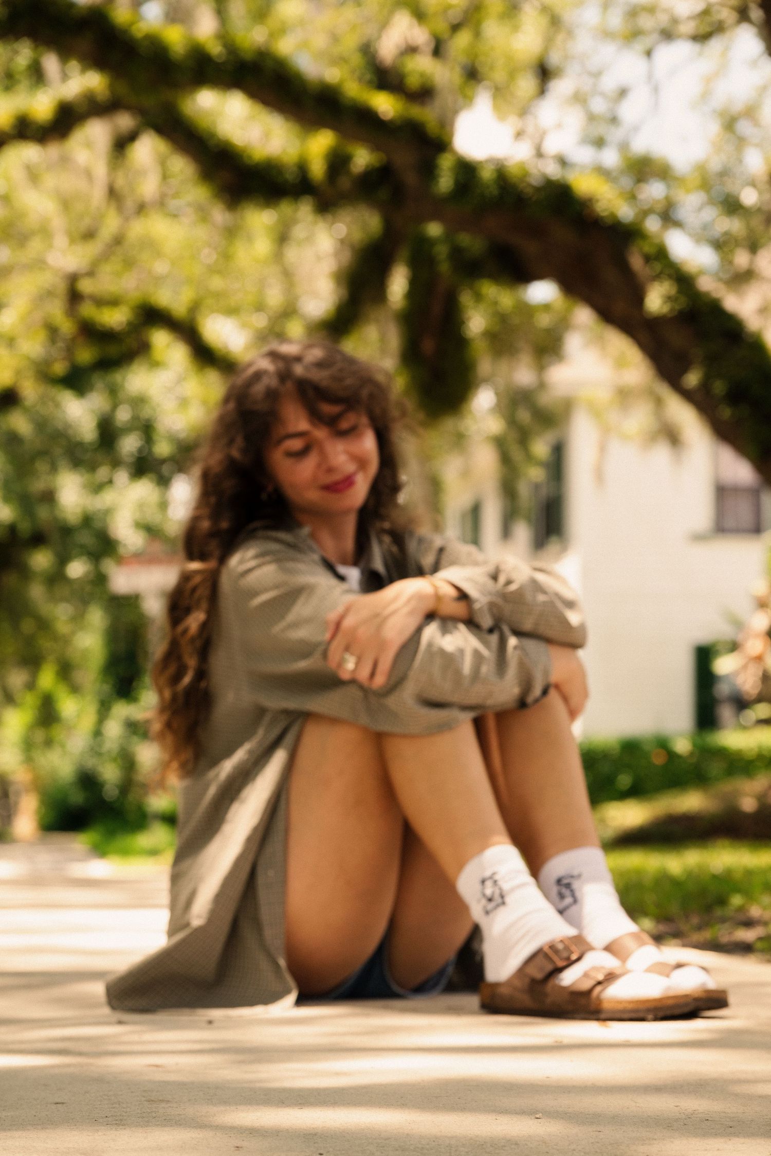 Someone sitting on ground in casual attire under shaded garden trees.