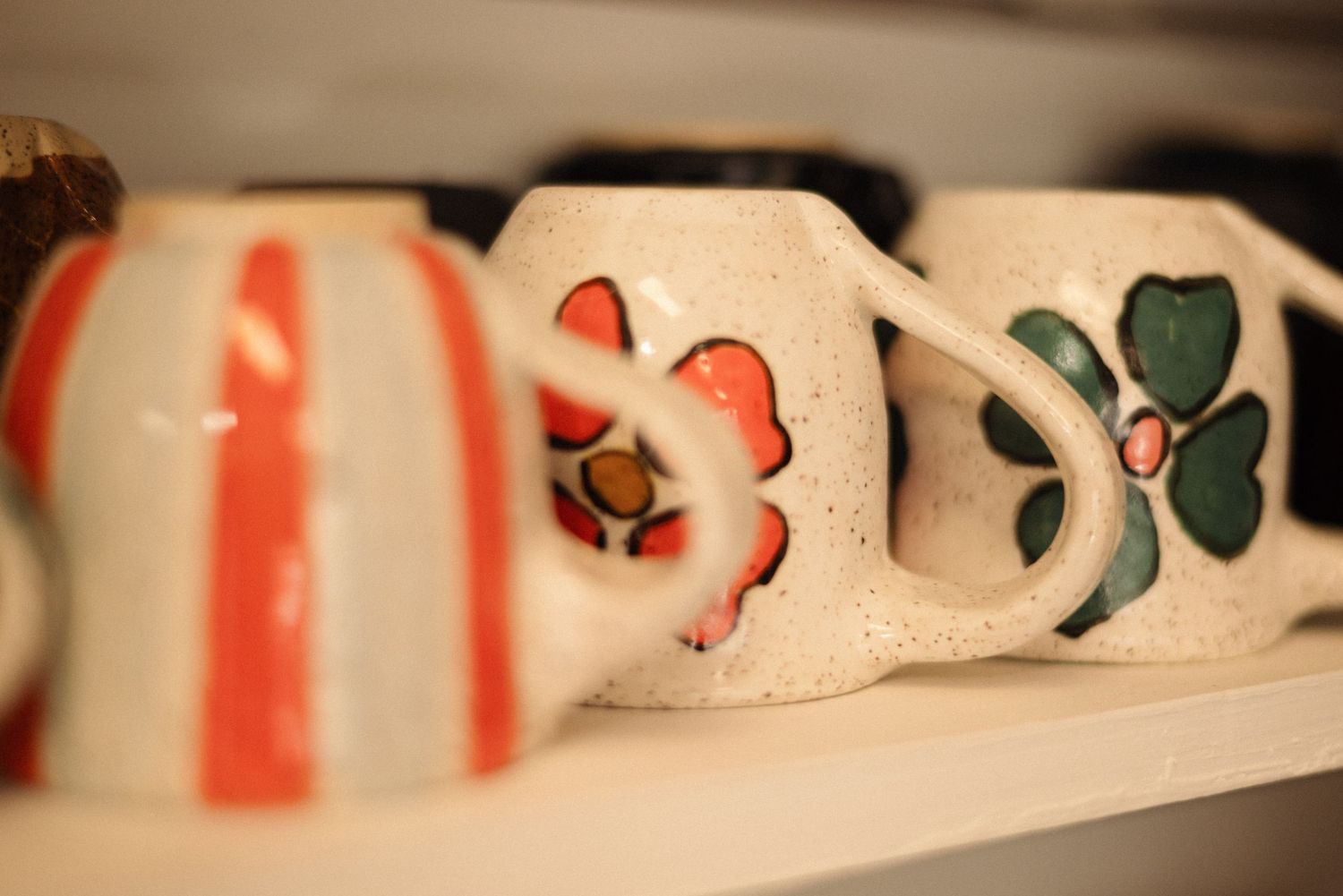 Decorative ceramic mugs with floral patterns displayed on a shelf.