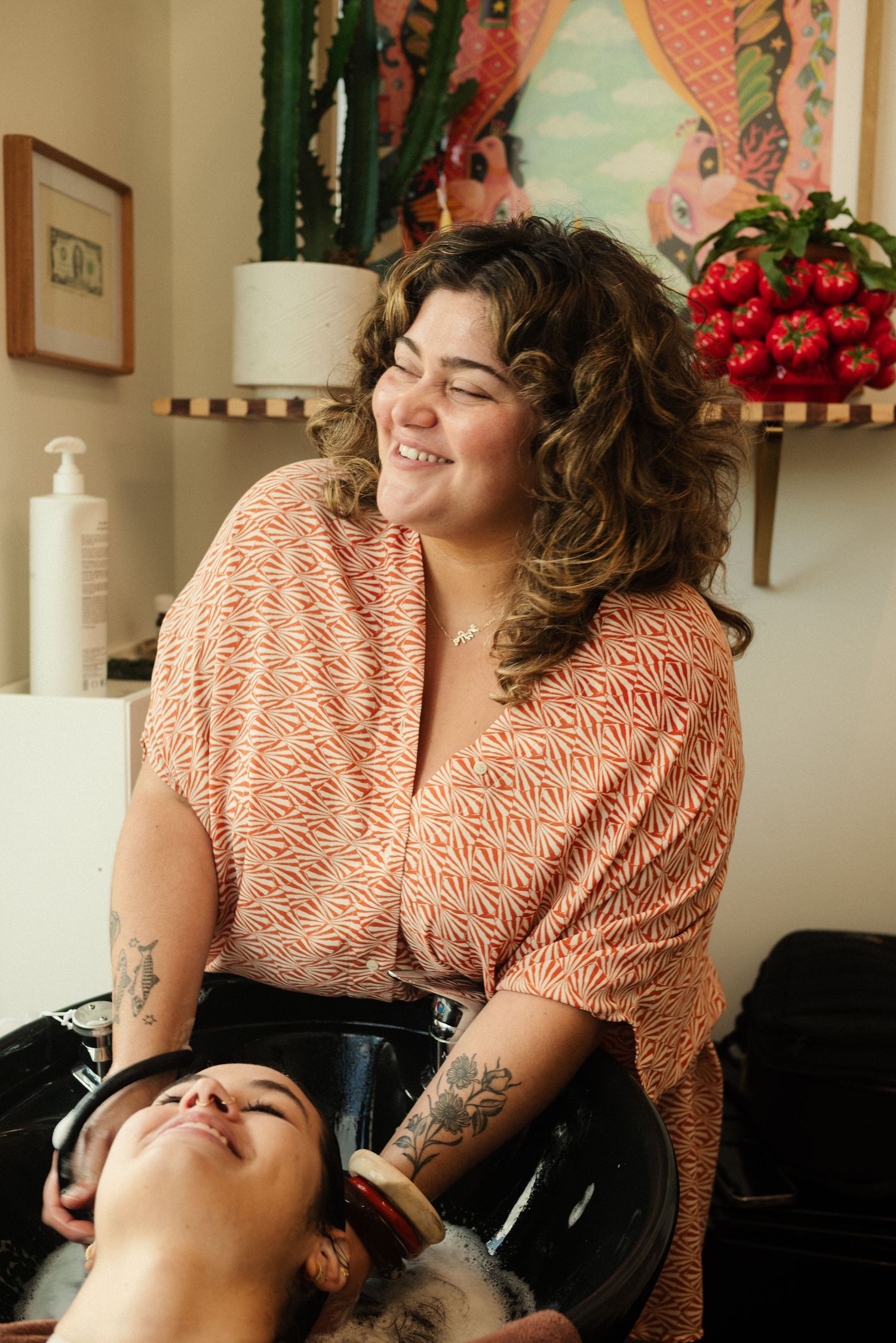 A hairstylist in a peach patterned dress working with a client in a salon chair.
