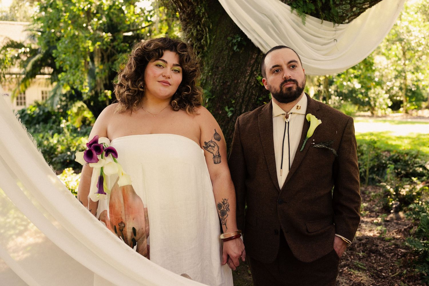 A couple poses together under white fabric draping at their outdoor wedding.