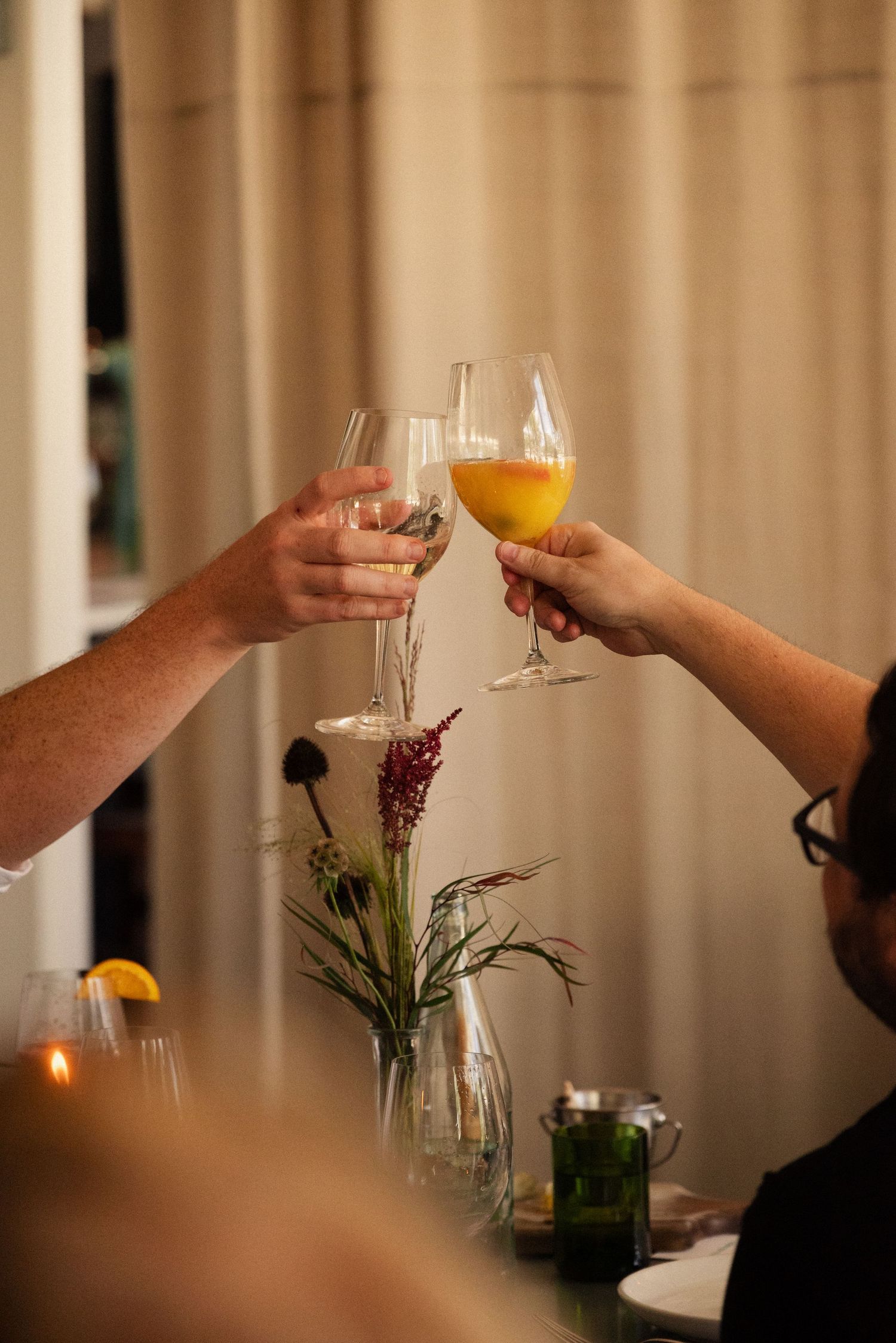 Two hands toasting with wine glasses over a floral centerpiece at an elegant dinner setting.