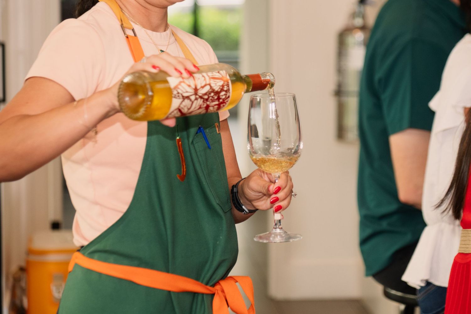 Someone in a green apron pouring wine into a glass during service.
