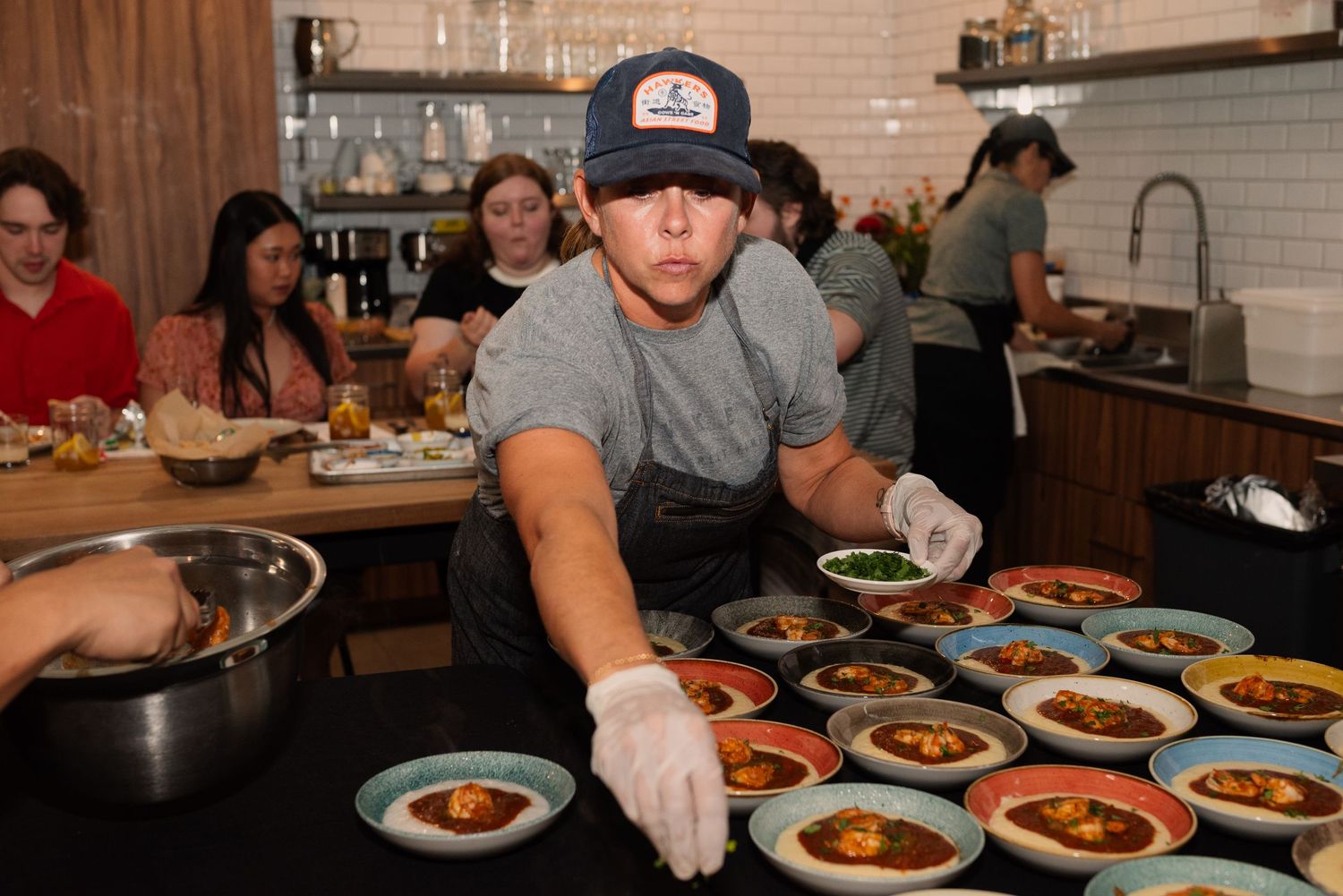 Restaurant worker plating multiple dishes at counter with various small plates of food.