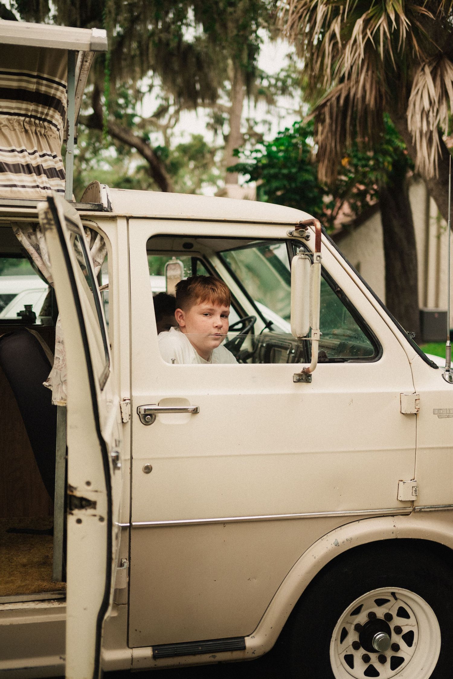 A vintage cream-colored car with someone sitting in the driver's seat.
