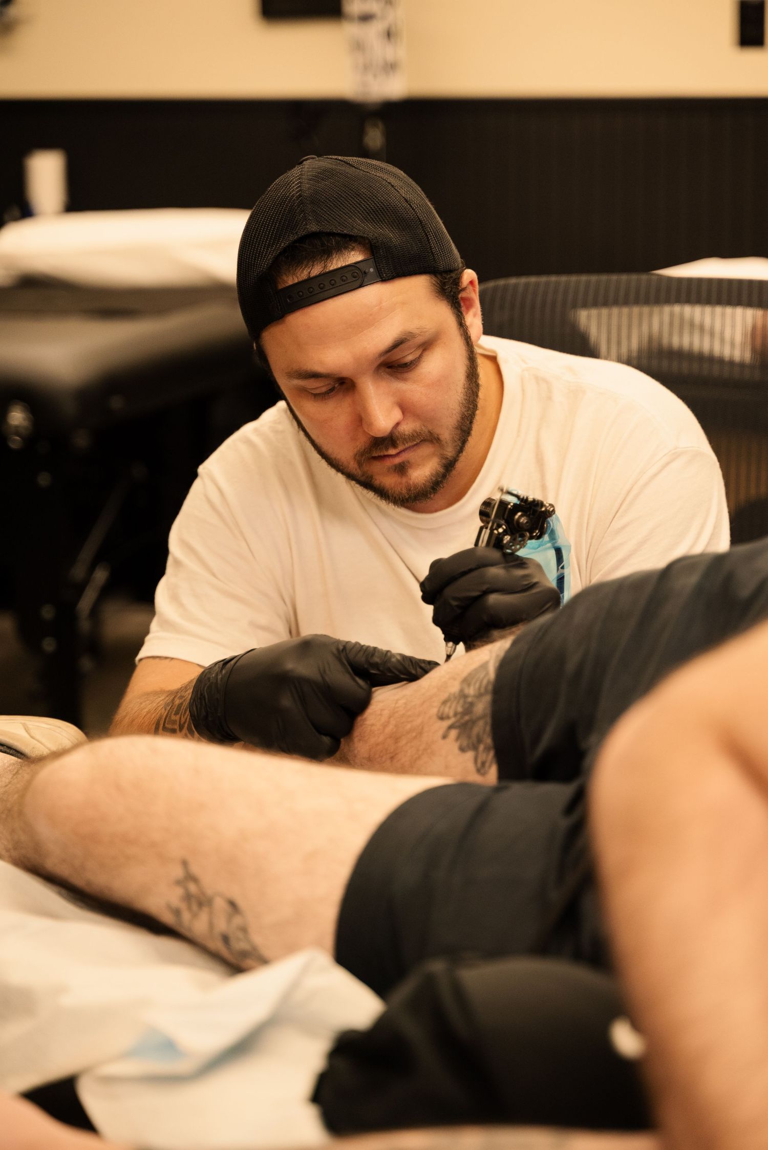 Artist concentrates while tattooing in a well-lit studio environment.