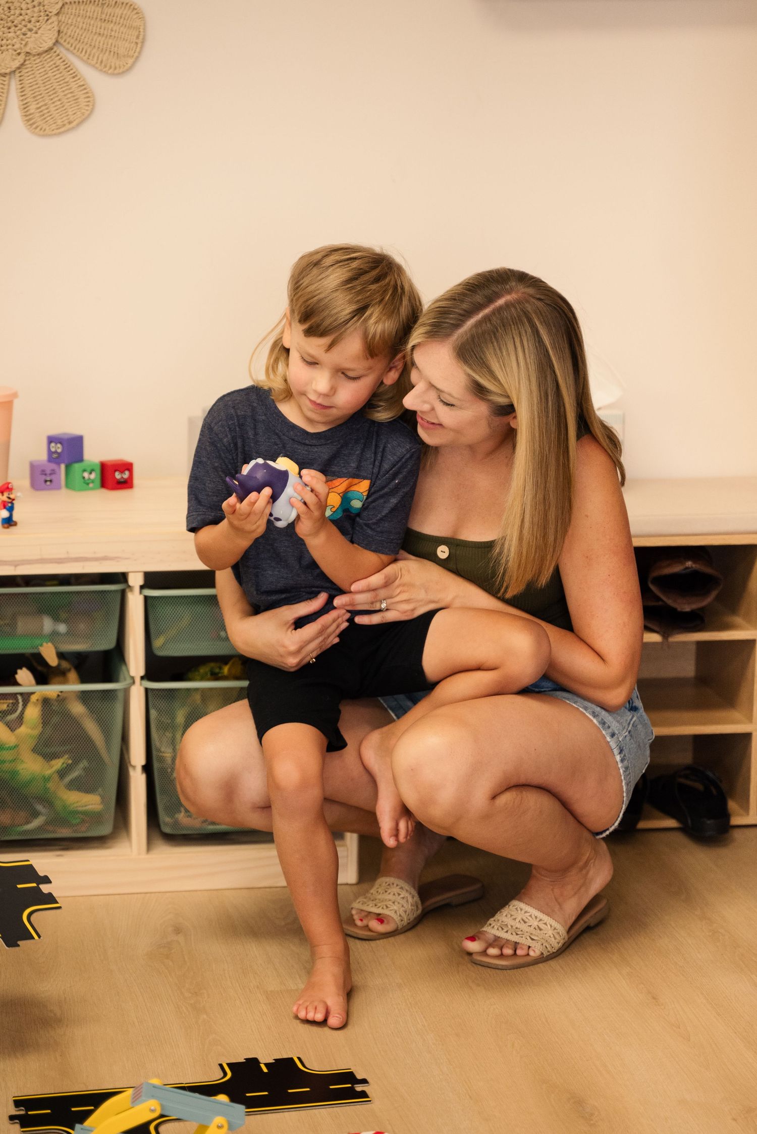 Parent and child playing together with toys on a light wooden floor.