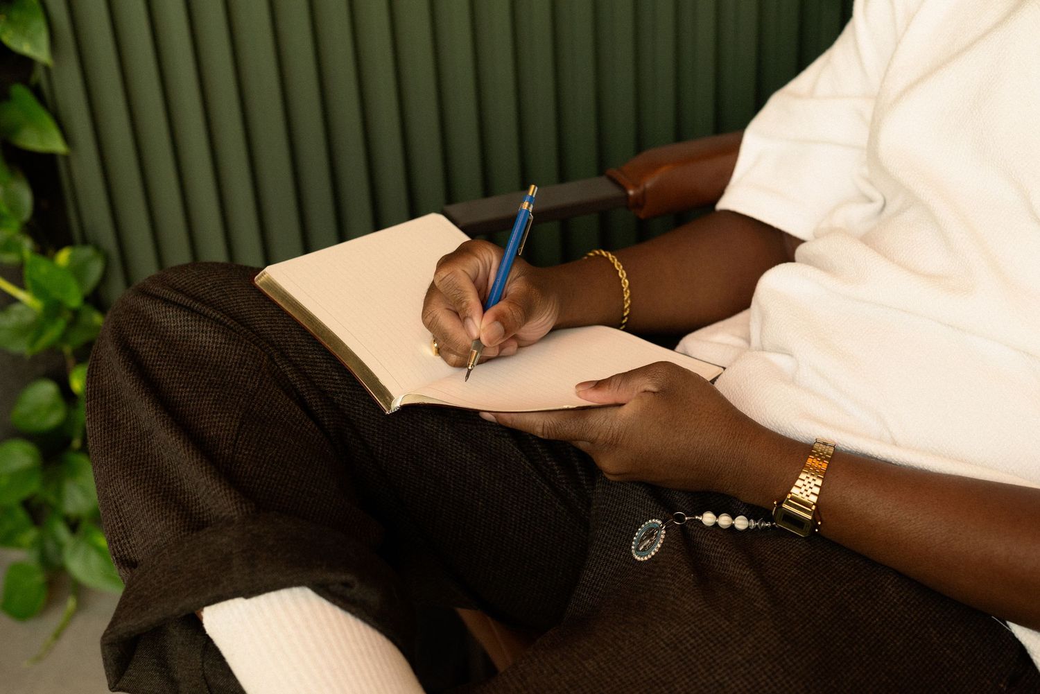 Person in white shirt taking notes in journal against green wall with plants.
