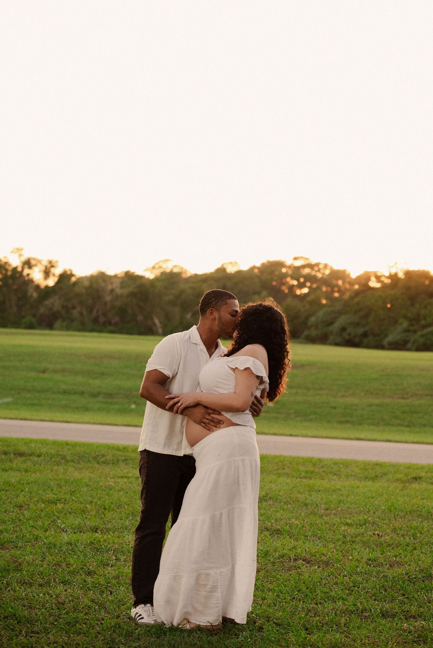 Loving couple poses together on grassy field during golden hour maternity shoot.