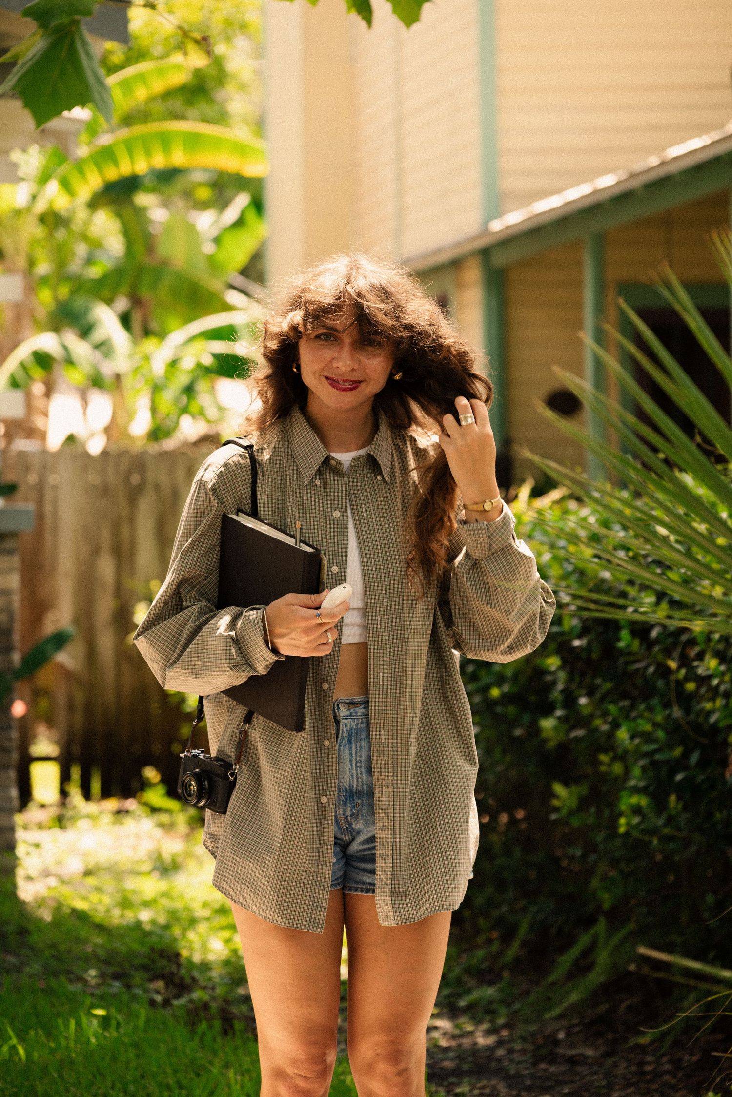 Casual summer outfit styled with oversized plaid shirt and shorts in a garden setting.
