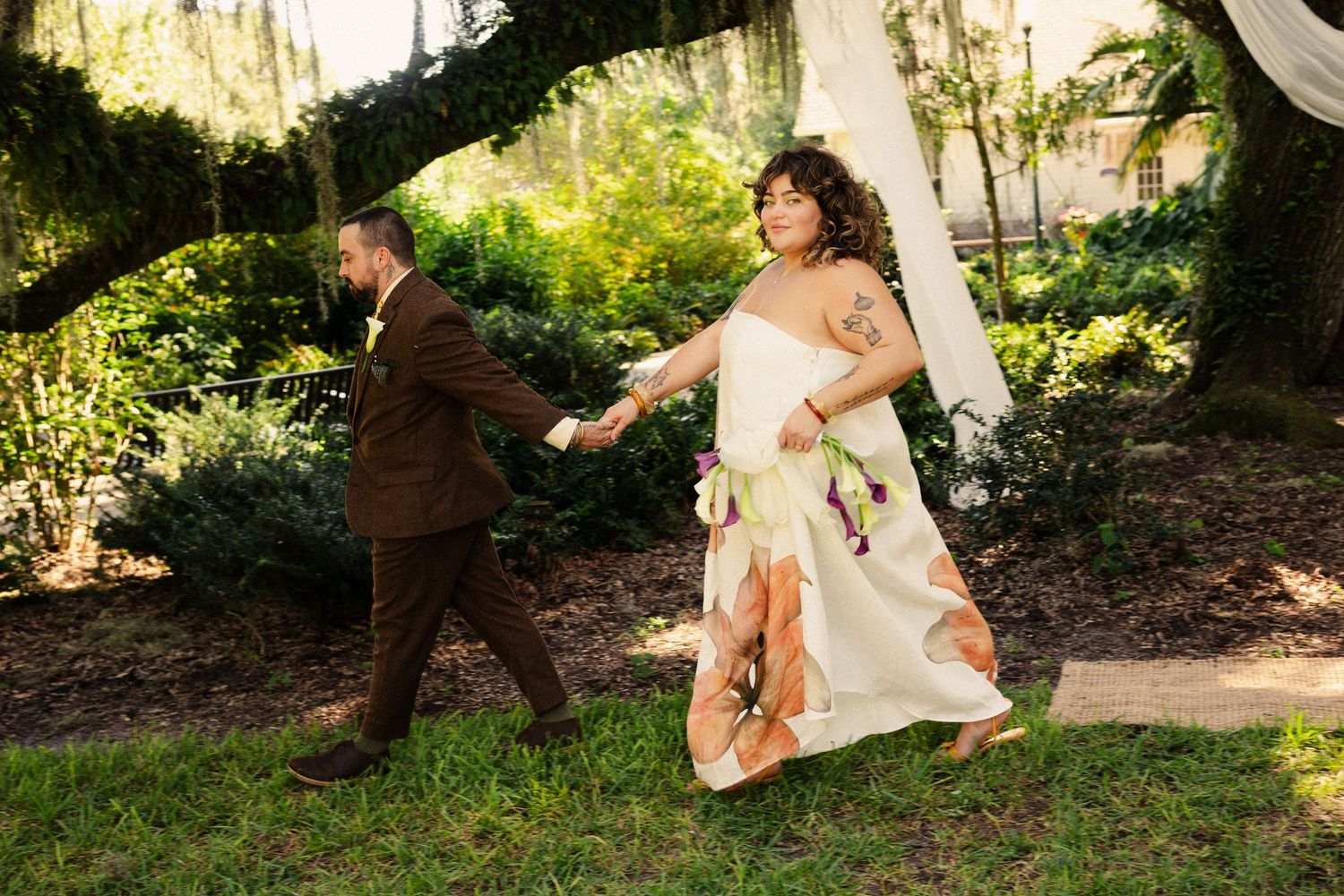 A couple playfully walks through an outdoor garden setting during their wedding.