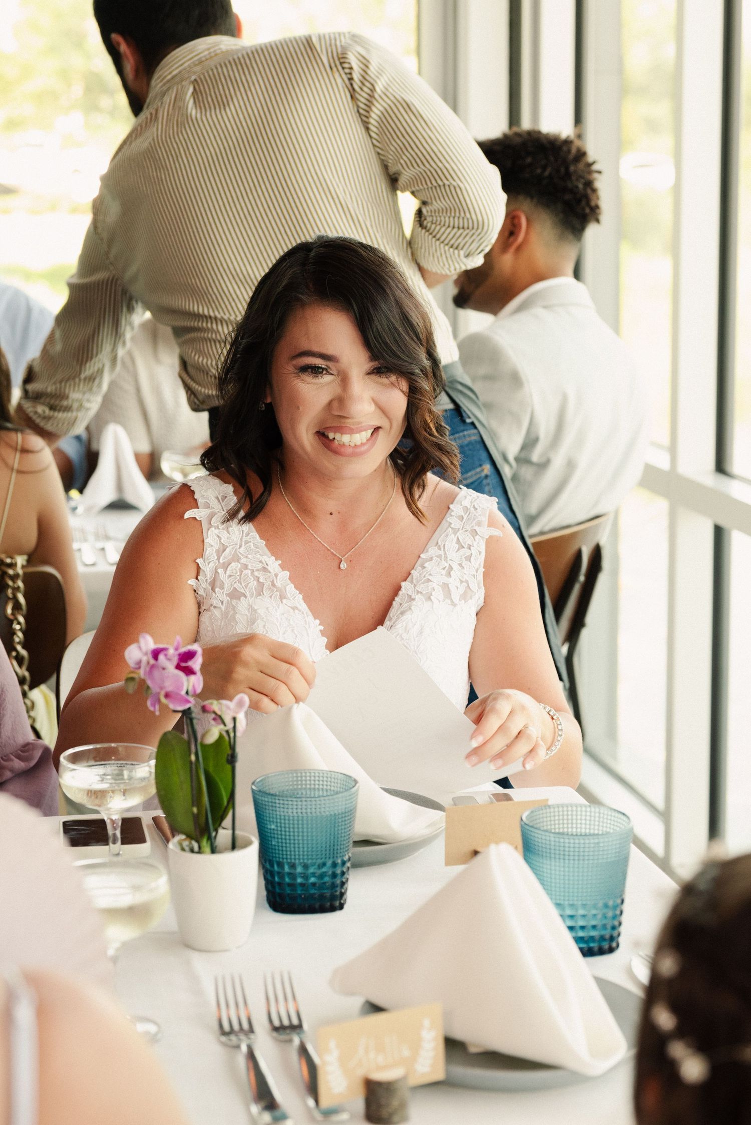 Wedding reception table setting with blue glassware and floral centerpieces in a bright indoor venue.