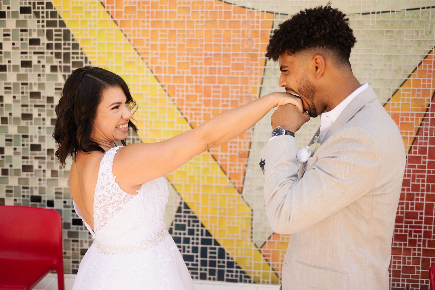 Dancing couple in wedding attire against a mosaic wall background.