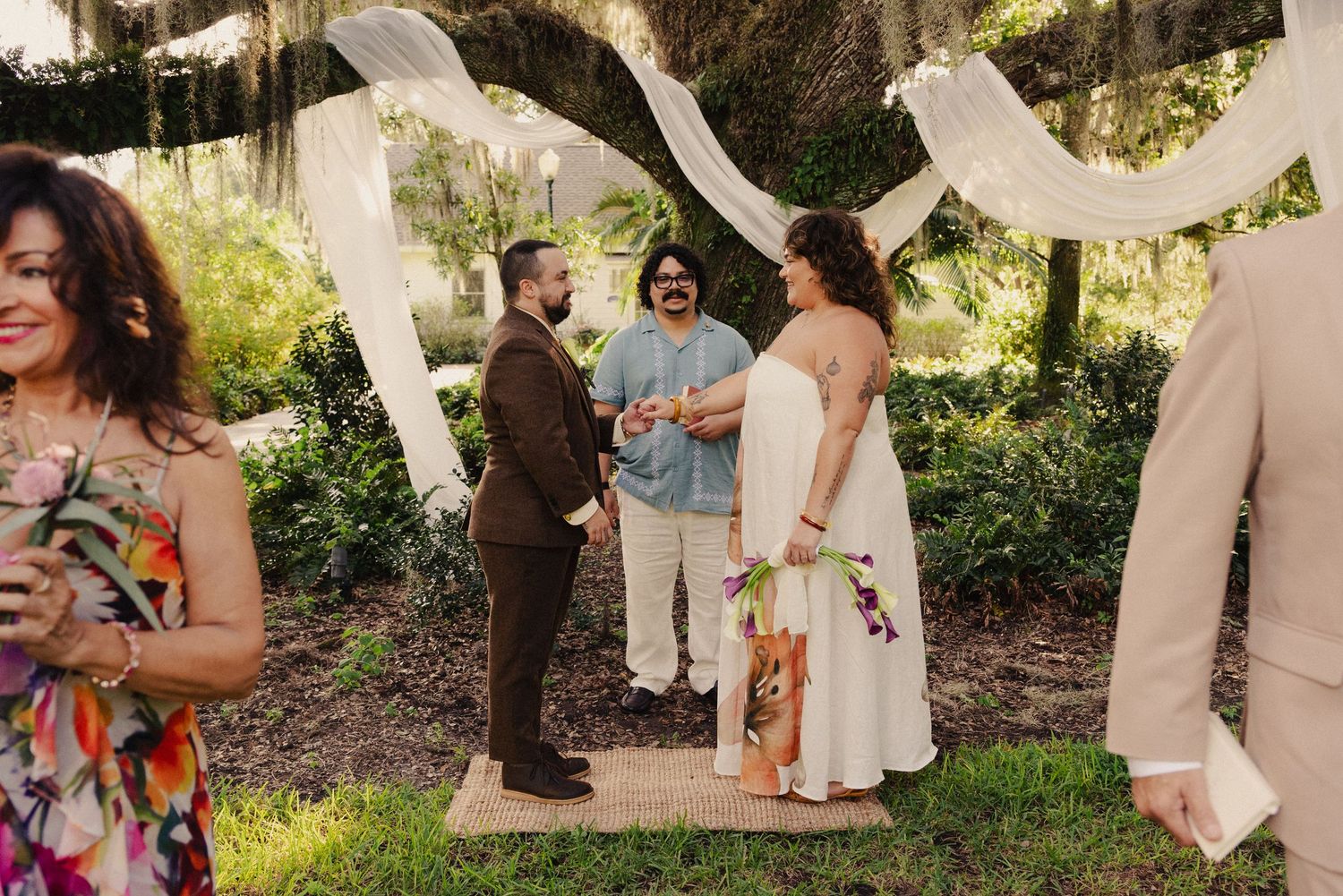 An outdoor wedding ceremony with white fabric draping and guests gathered in a garden setting.
