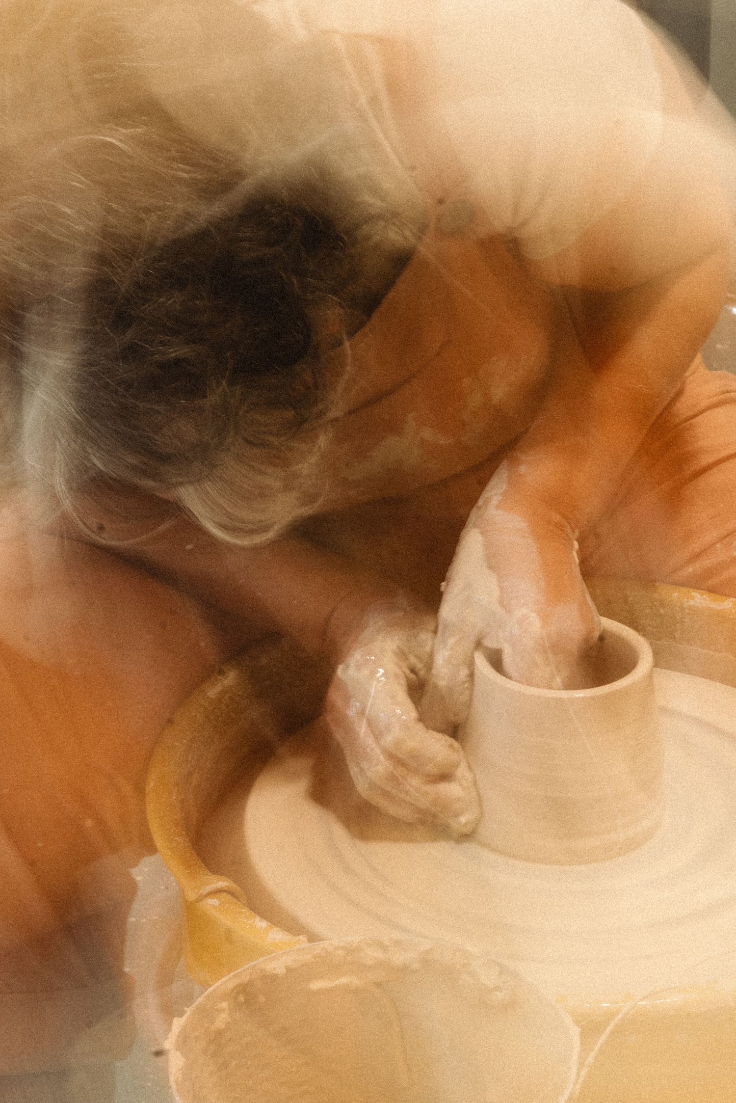 Artistic soft-focus image of a potter working on a clay vessel.