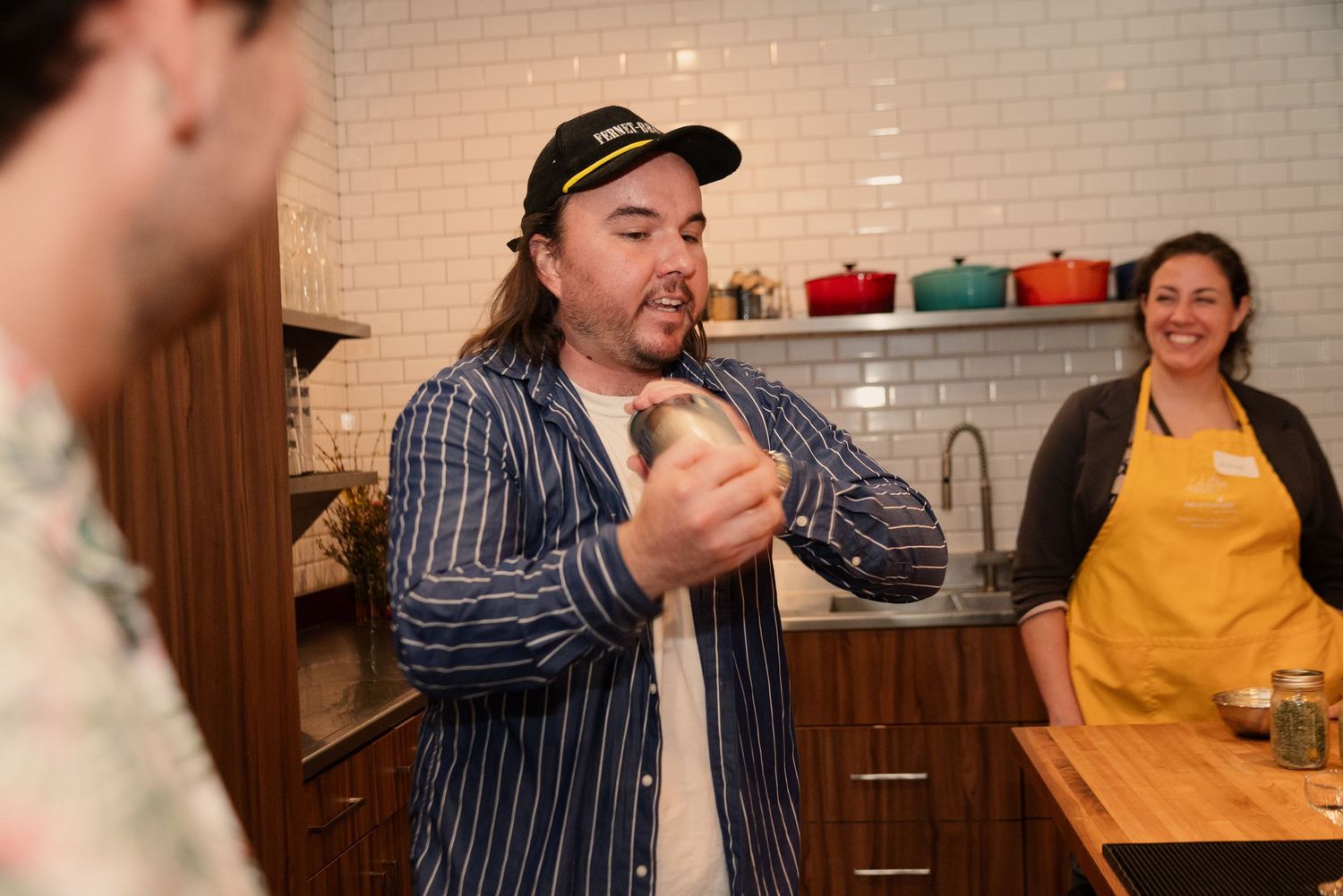 People gathered around a wooden bar counter during a mixology workshop with drinks and ingredients.