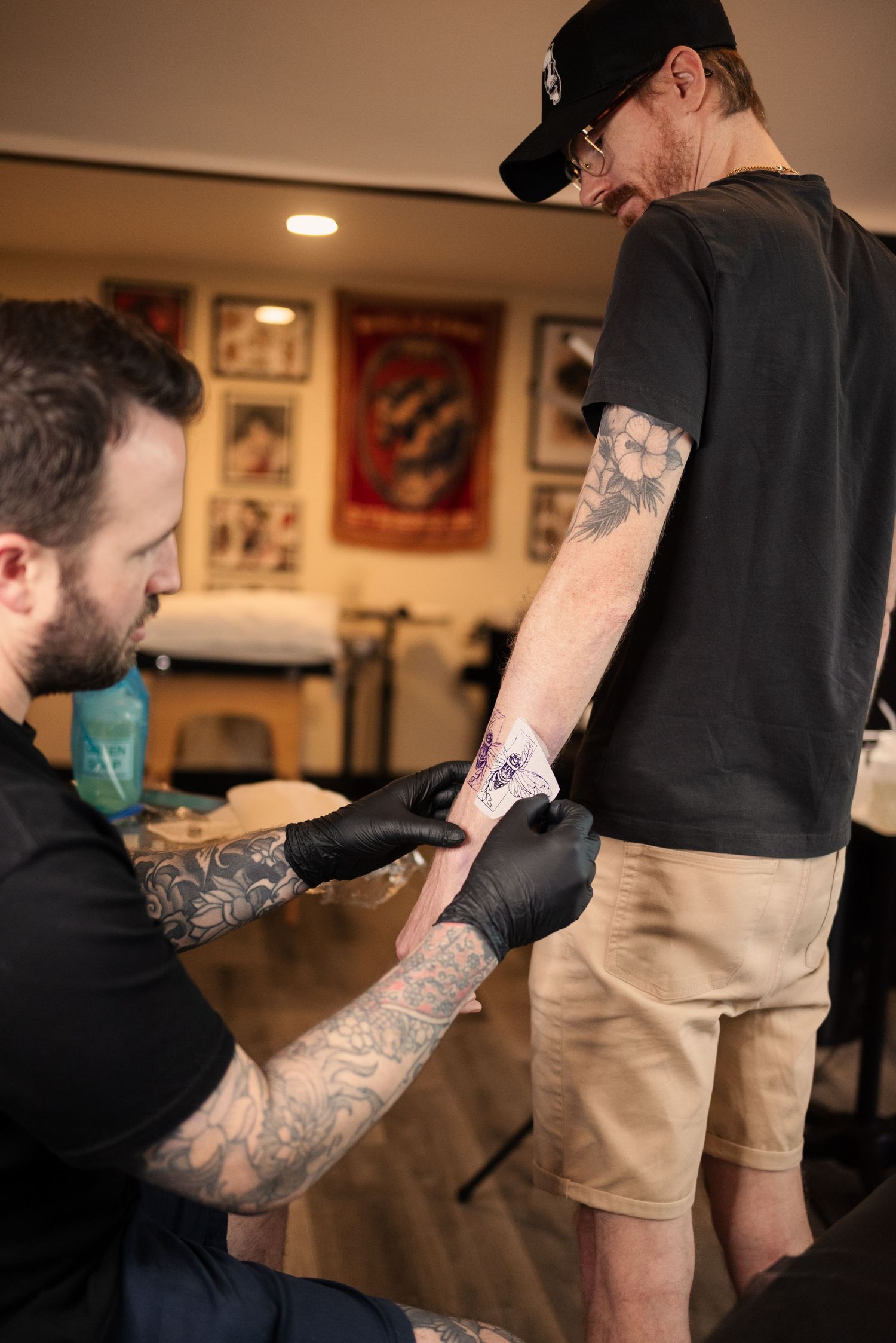 Tattoo artist with sleeve tattoos working on a client in studio setting.