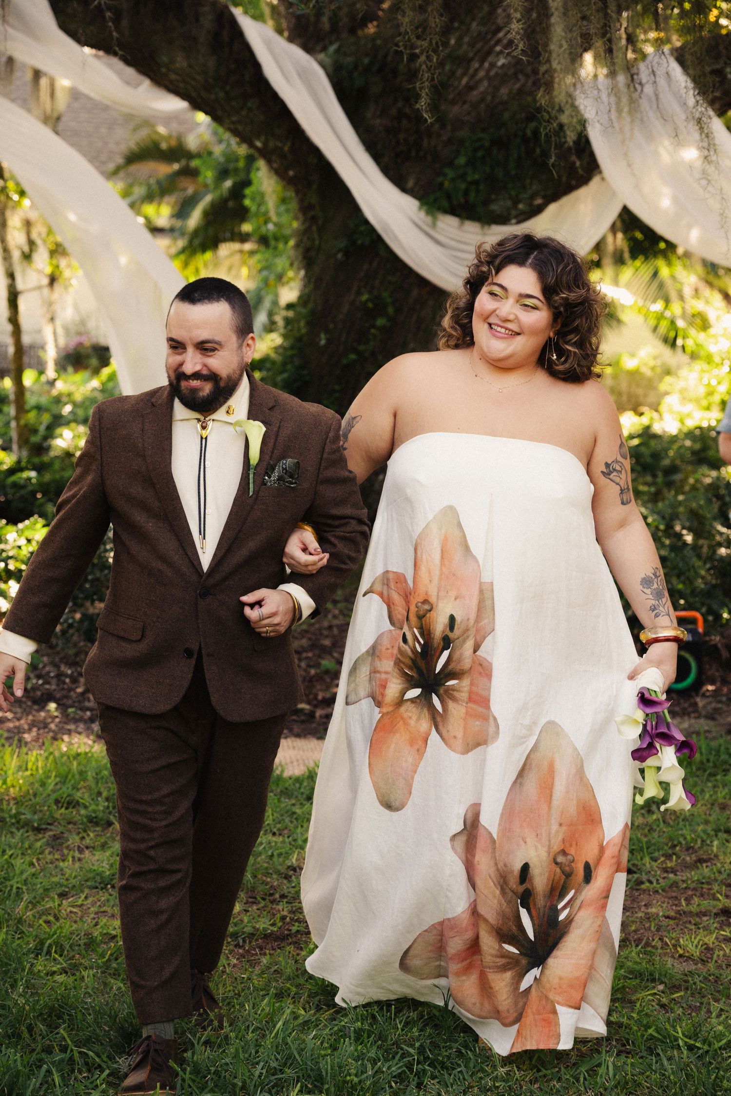 Joyful couple walking together outdoors, bride wearing floral-printed white dress.