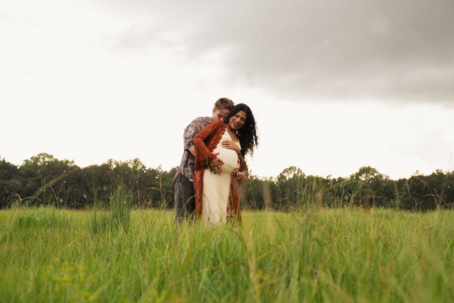 Silhouettes of people embracing in a grassy meadow with trees in the background.