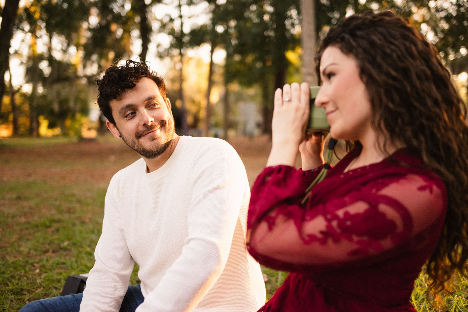 A couple in burgundy and white clothing share tender moments outdoors at sunset.