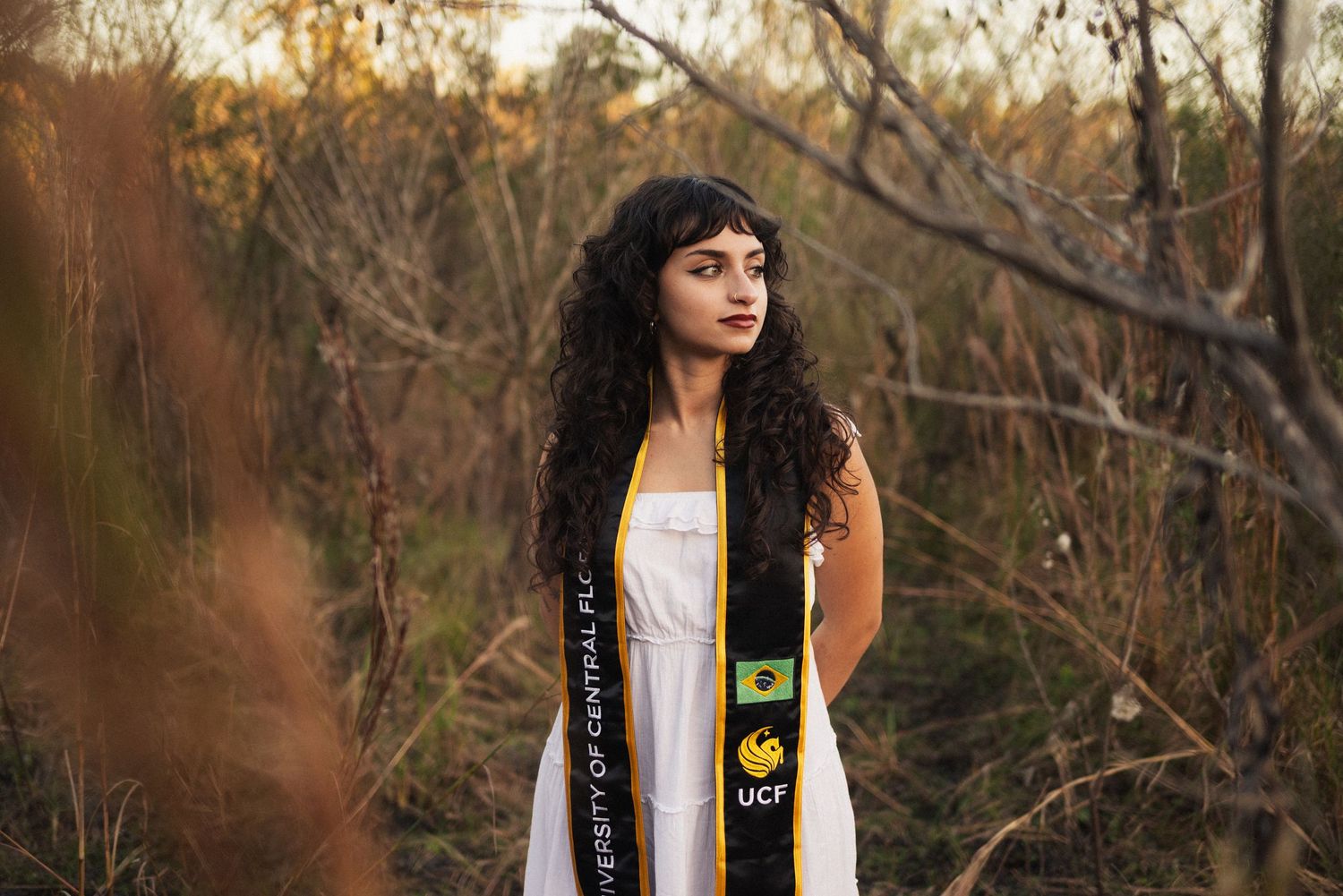 Outdoor portraits featuring a white dress and graduation stole against a wooded backdrop.