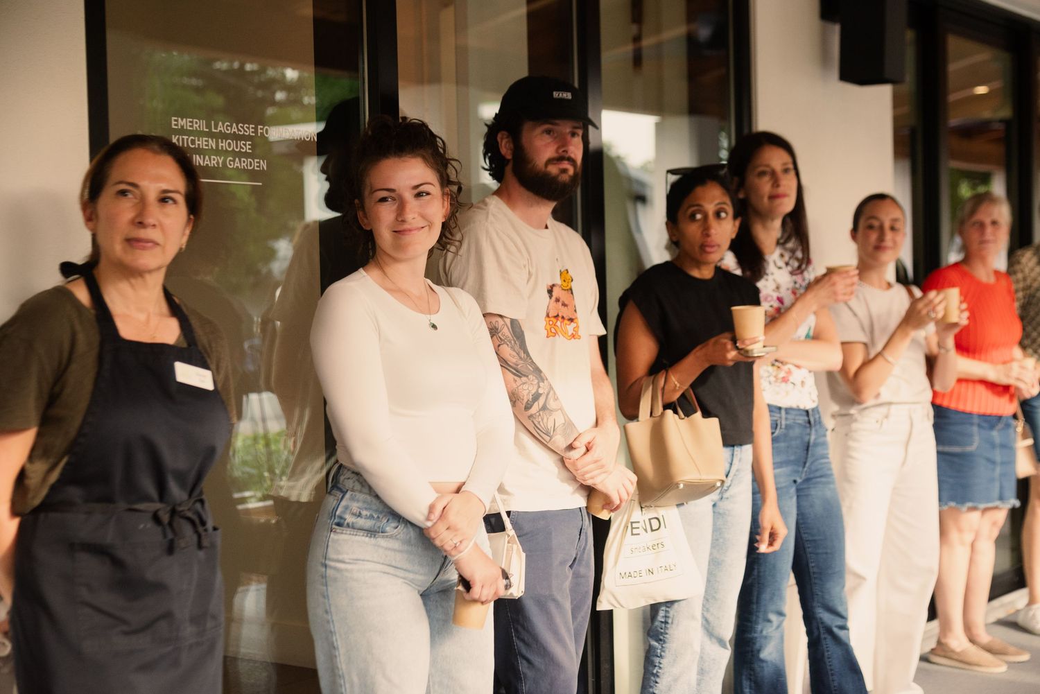 Line of people standing outside a building wearing casual attire and aprons.