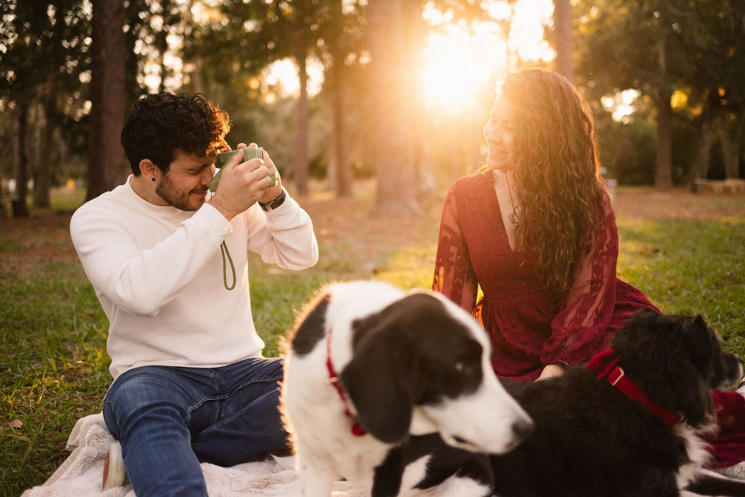 A couple and their dogs share a playful moment in a park during sunset.