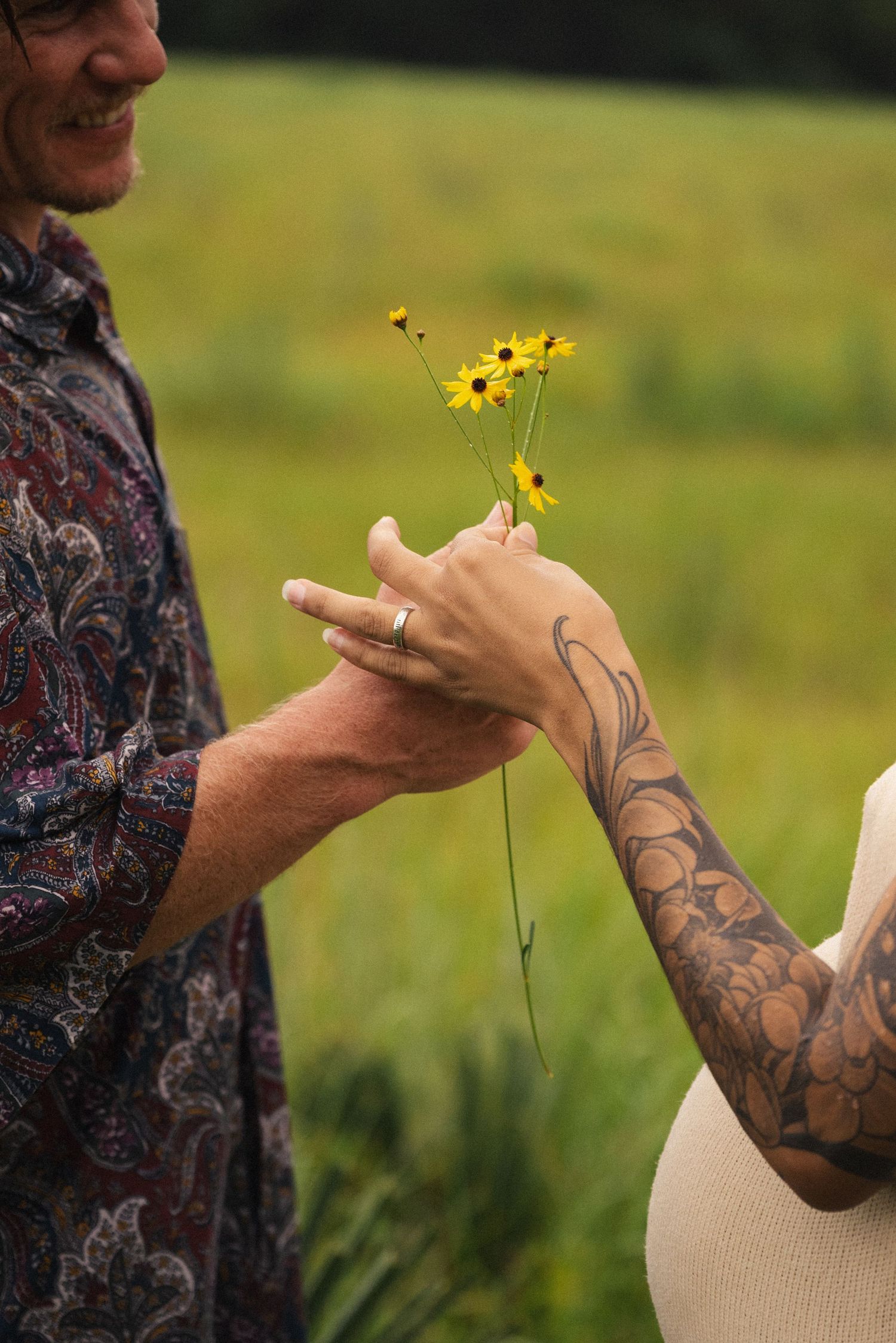 Tattooed arms holding delicate yellow wildflowers in a sunny field.