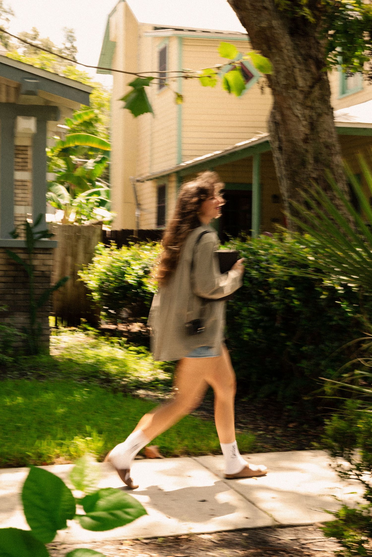 Figure walking along a tree-lined path in front of vintage houses.