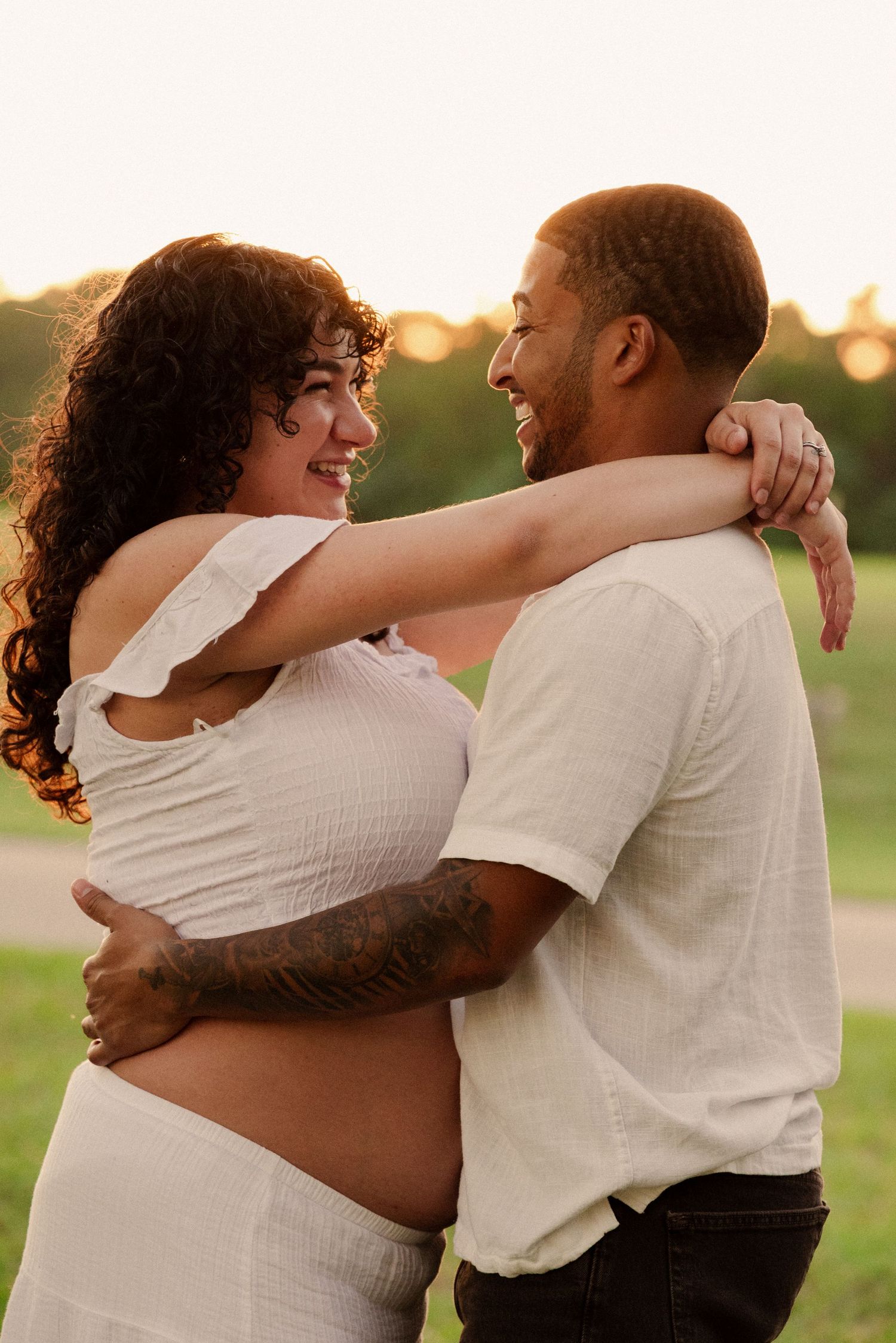 Sunset maternity session shows couple sharing tender moments in white outfits.