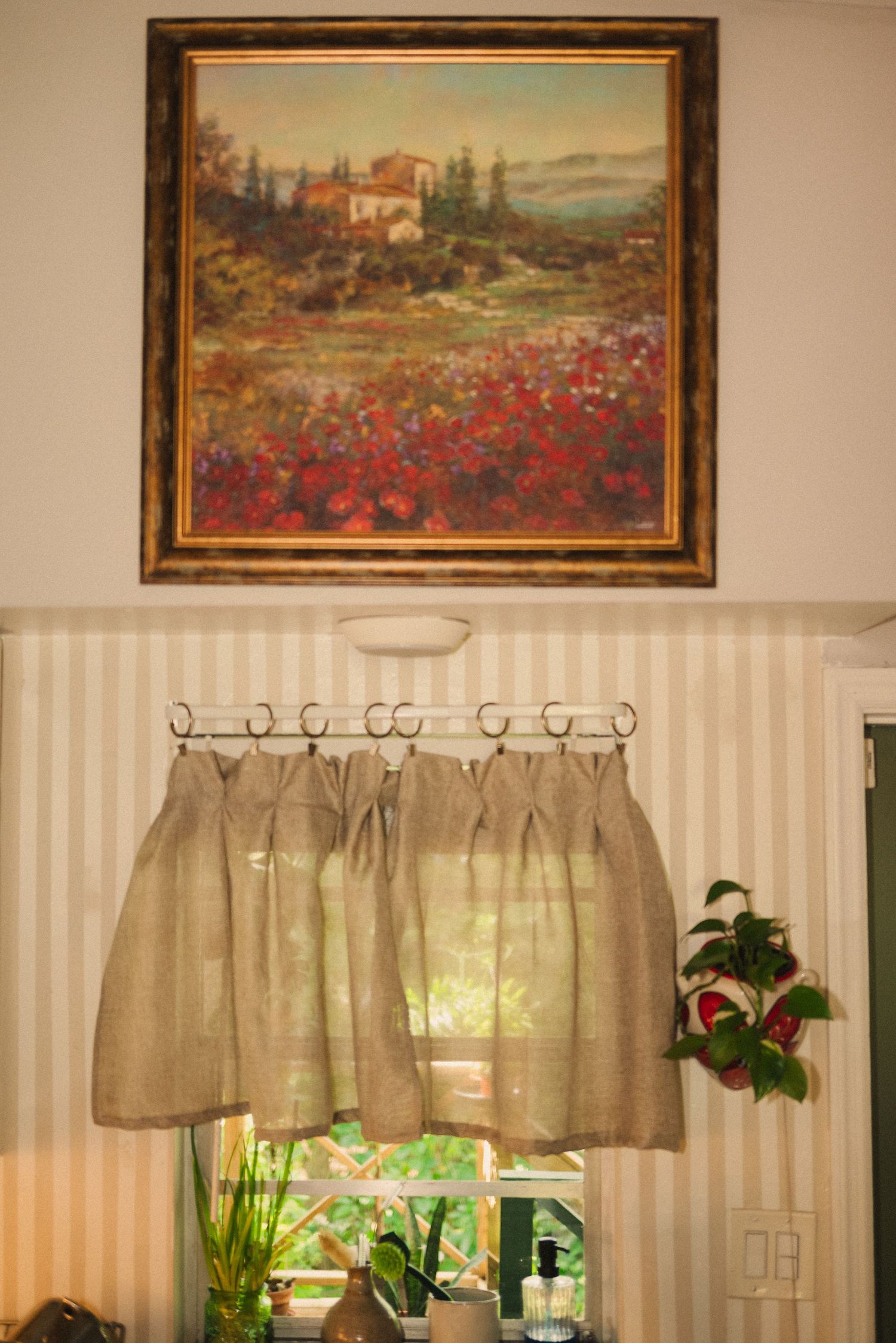 A wall decorated with framed landscape paintings and burlap curtains in a rustic interior setting.