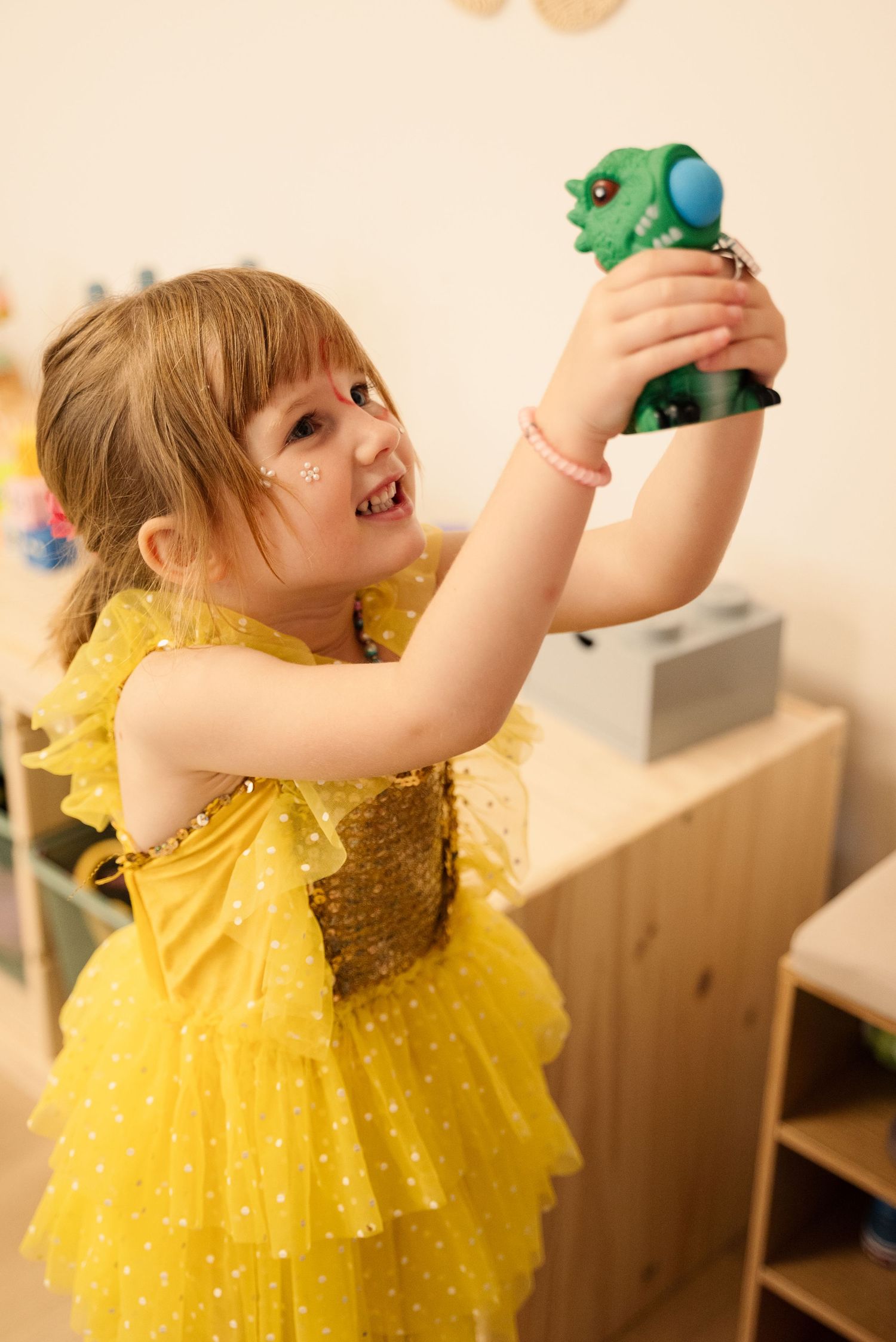 Child in yellow sparkly dress playing with toys during indoor playtime.