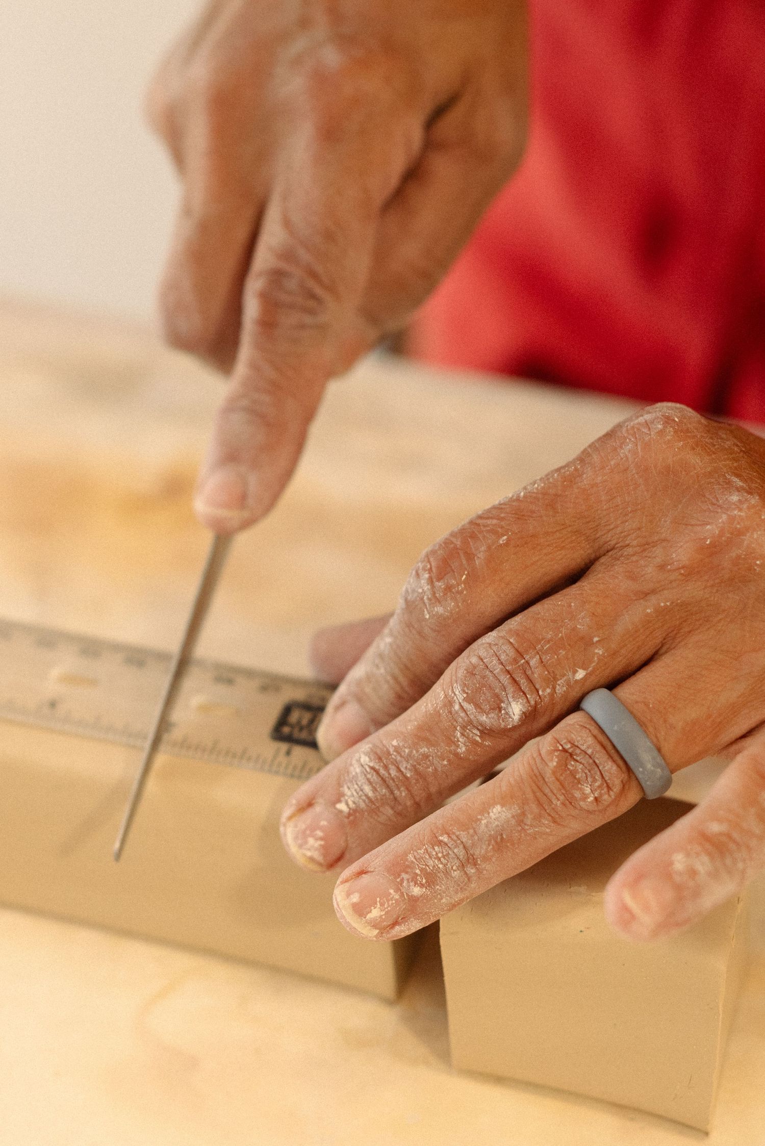 Dusty hands using a ruler and tool to measure clay work.