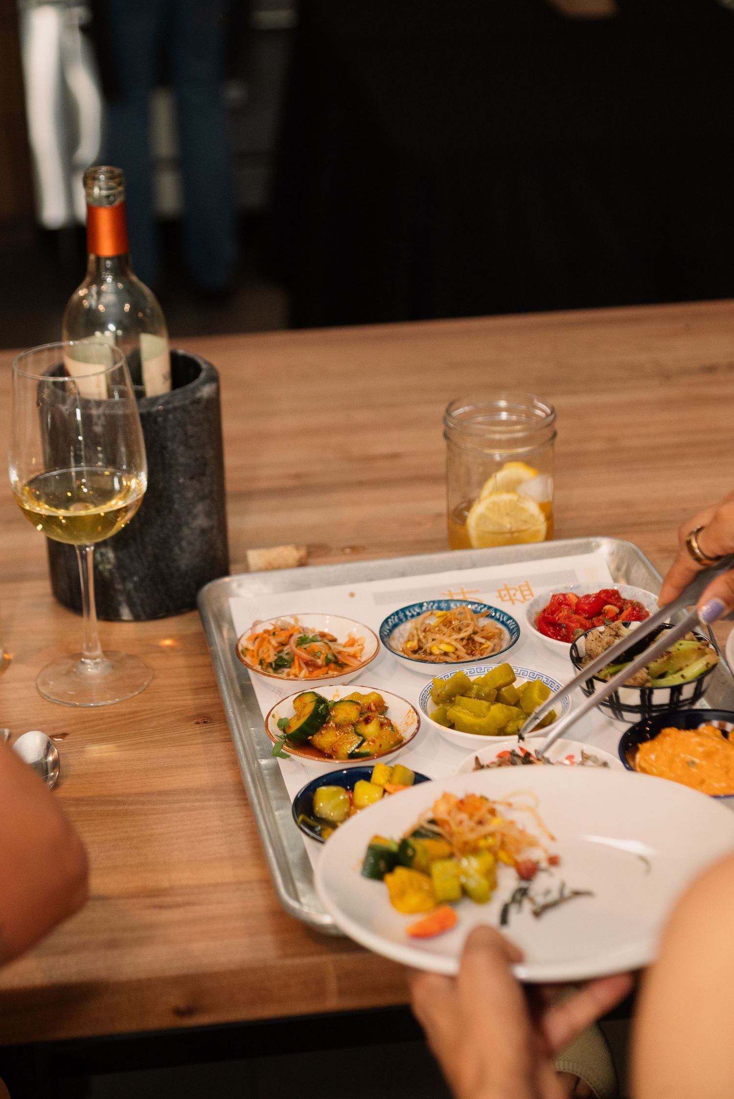 A tasting plate with various small portions of food next to a glass of white wine on a wooden table.